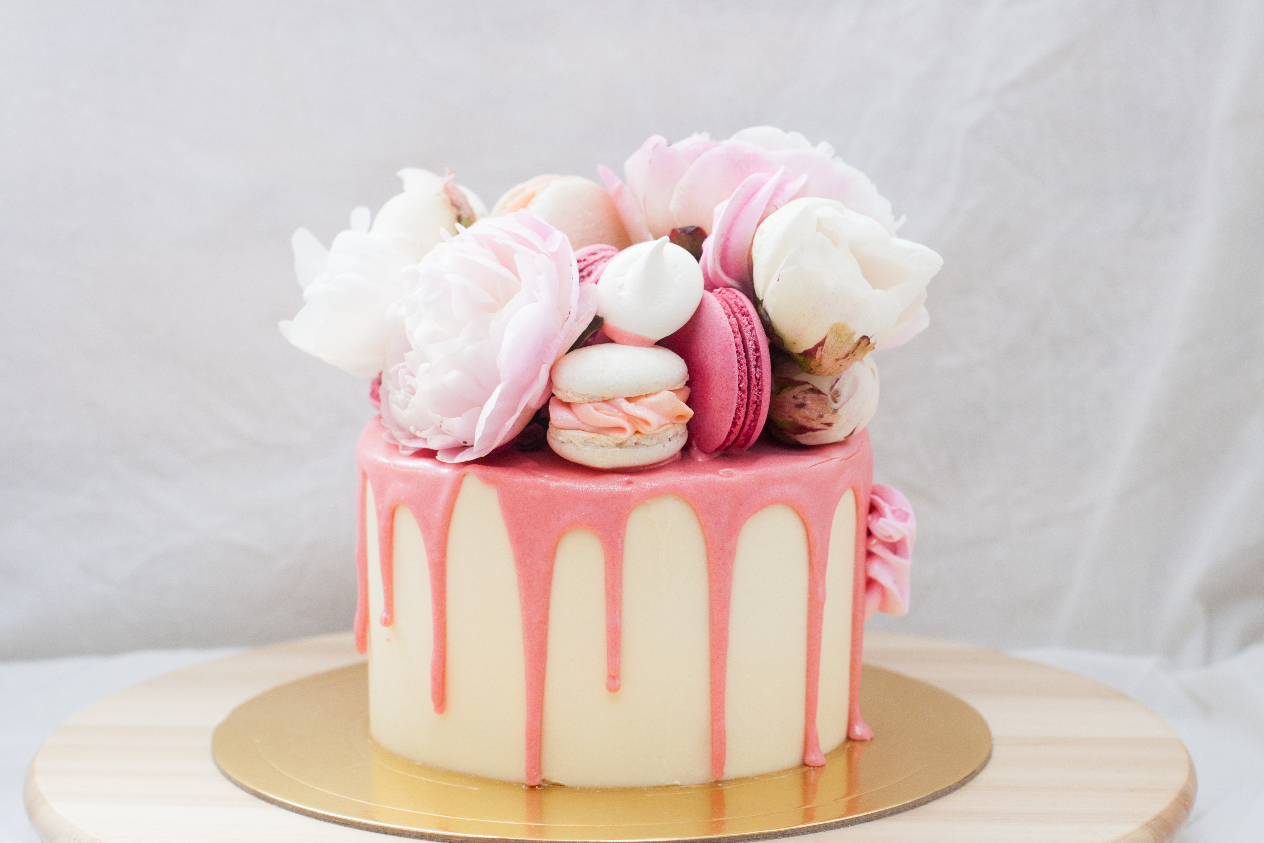 Petit gâteau d'anniversaire avec du chocolat rose fondu, des pivoines fraîches, des macarons et des meringues sur fond blanc | Source : Getty Images