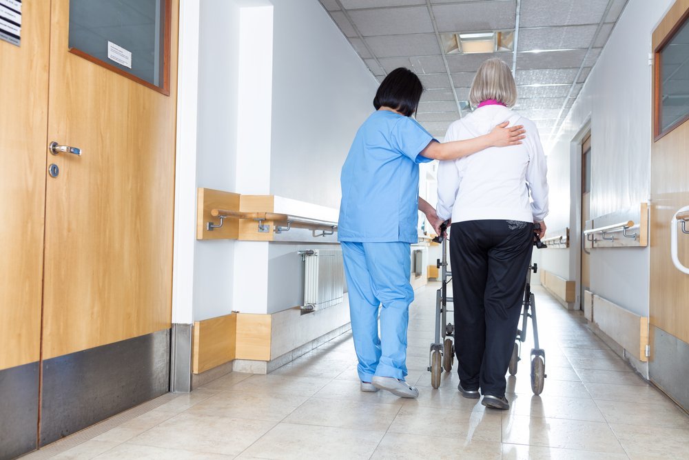 Une infirmière aide une pensionnée à marcher dans les couloirs d'une maison de retraite. | Shutterstock