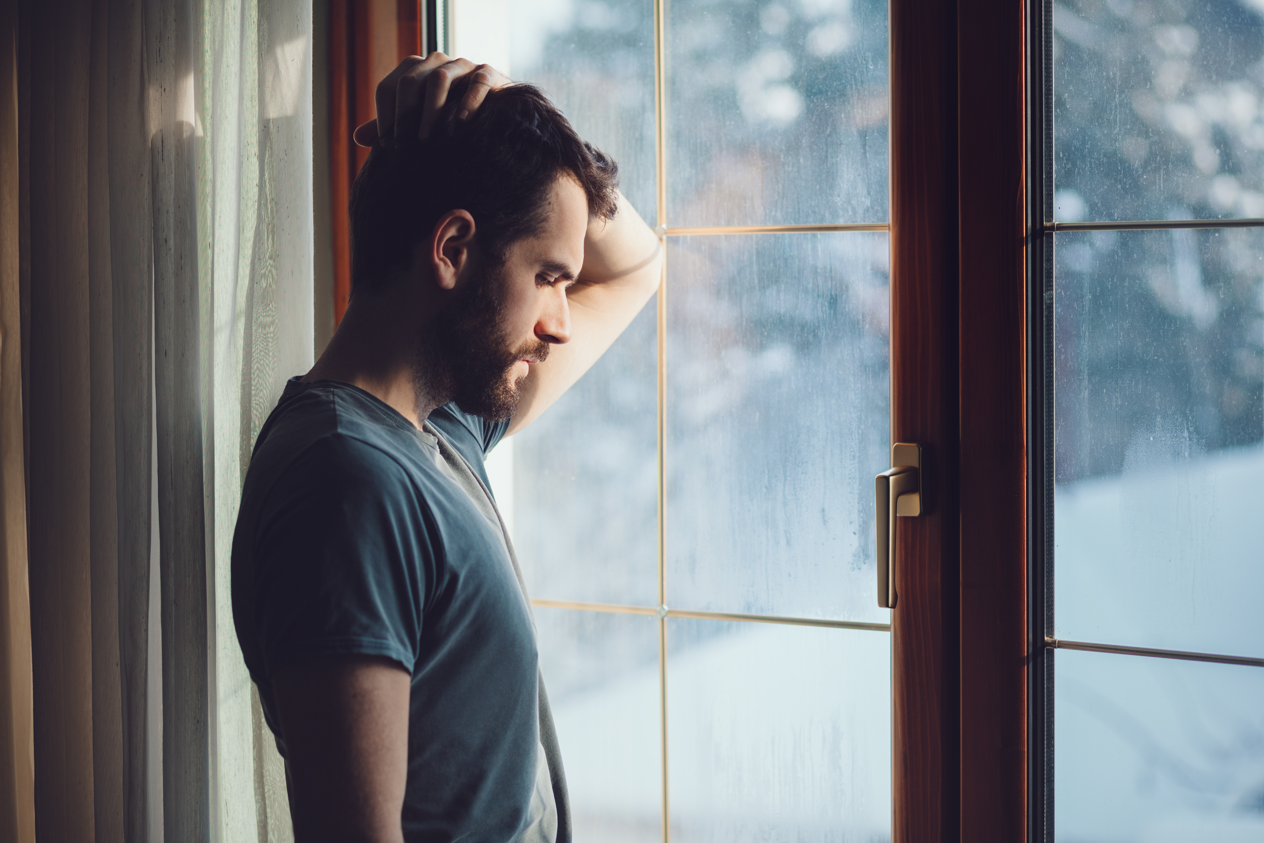 Un homme se tient debout près d'une fenêtre, la main sur la tête. | Source : Shutterstock