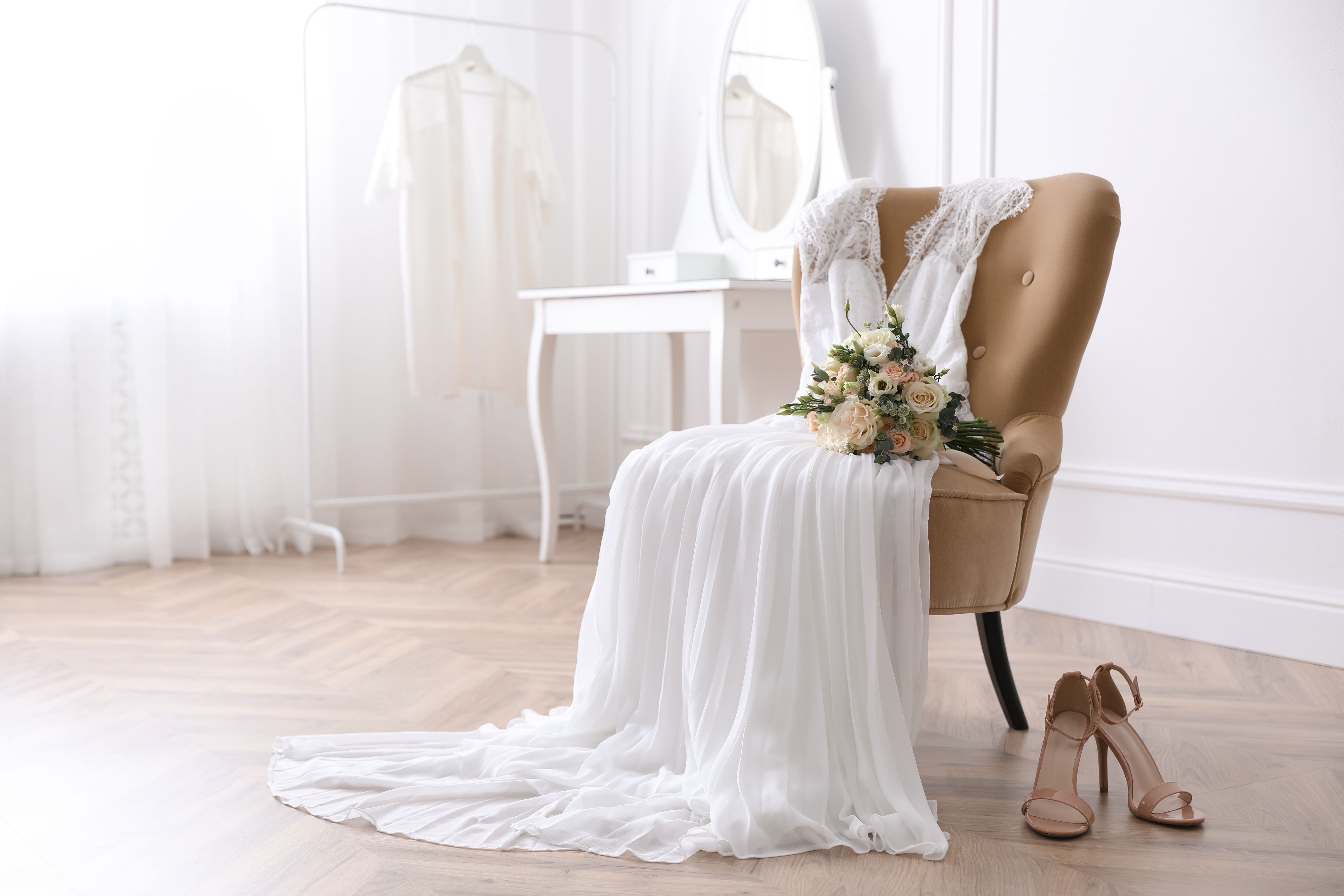 Une robe de mariée blanche sur une chaise et des chaussures à talons hauts sur le sol. | Source : Shutterstock