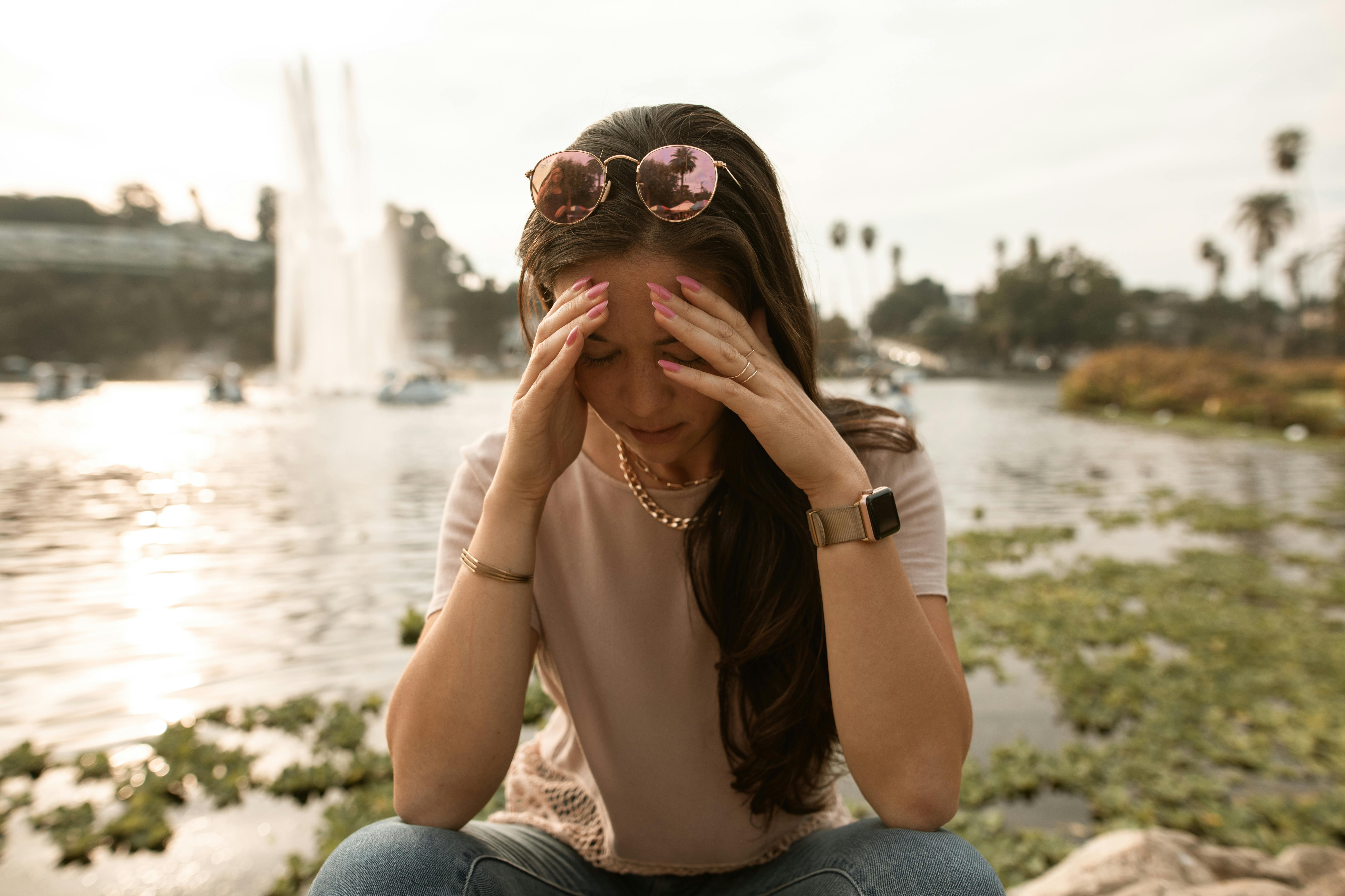 Une femme en détresse assise au bord d'un lac et se touchant le visage en signe de désespoir | Source : Pexels
