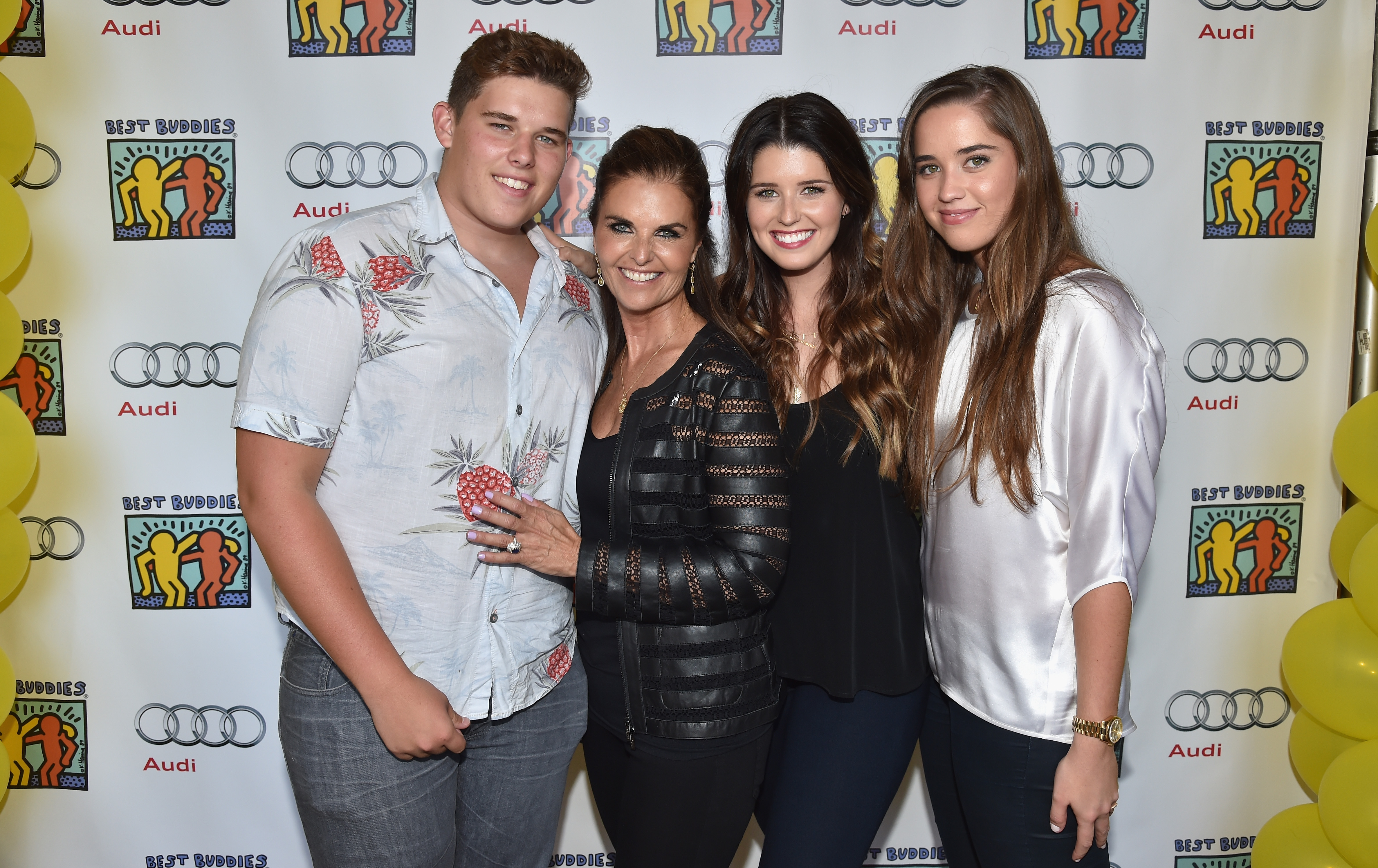 Christopher pose avec sa mère, Maria Shriver, et ses sœurs Katherine et Christina lors d'un événement à Beverly Hills. Vêtu d'une chemise boutonnée claire avec un motif de fruits audacieux et d'un jean gris, il se tient debout avec assurance et un sourire, ses cheveux courts soigneusement coiffés et sa corpulence visiblement plus importante à l'époque.