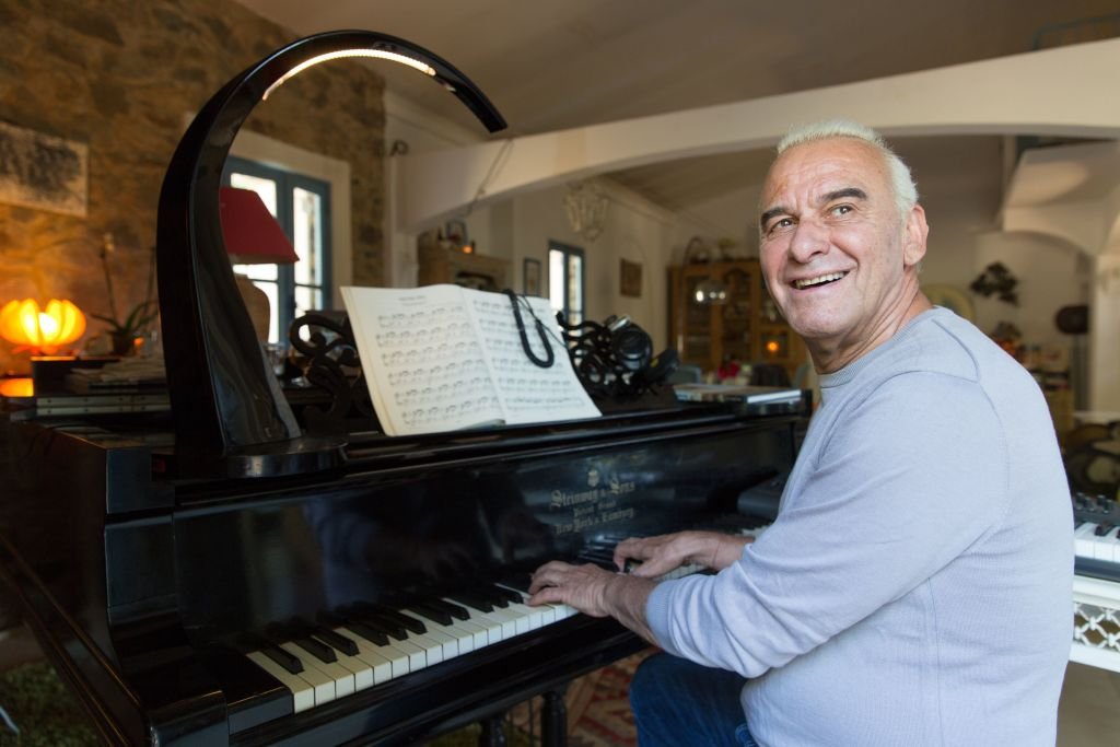 Le chanteur français Michel Fugain joue du piano chez lui le 30 juin 2013 à Corbara, en Corse. | Photo : Getty Images