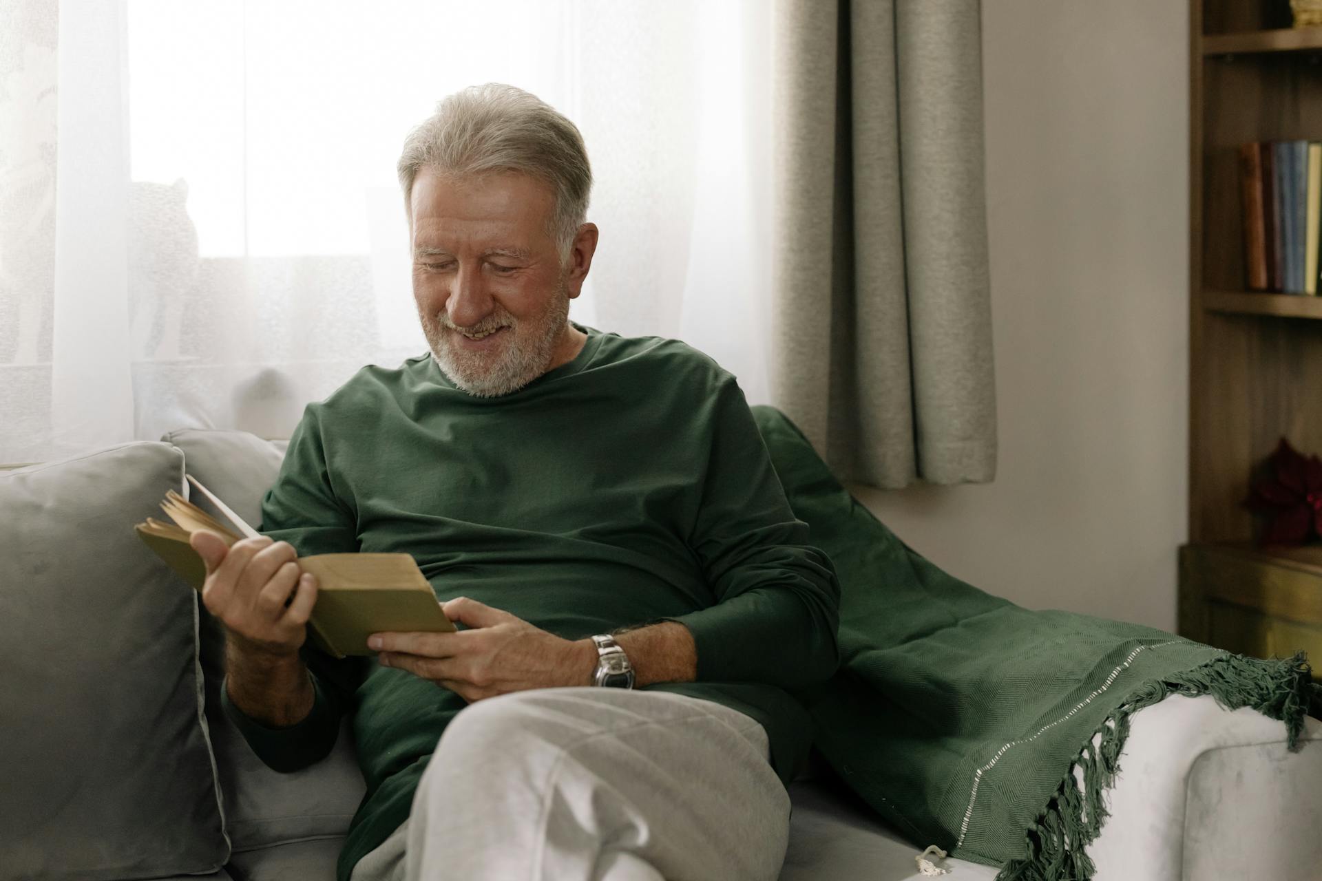 Un homme âgé souriant lisant un livre | Source : Pexels