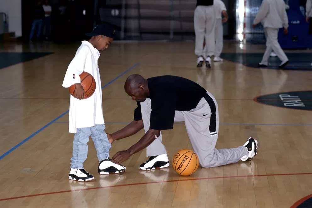 Michael Jordan fait les lacets de son fils lors d'un entraînement pour un tournoi de basket à Paris, en France, en 1998. | Source : Getty Images