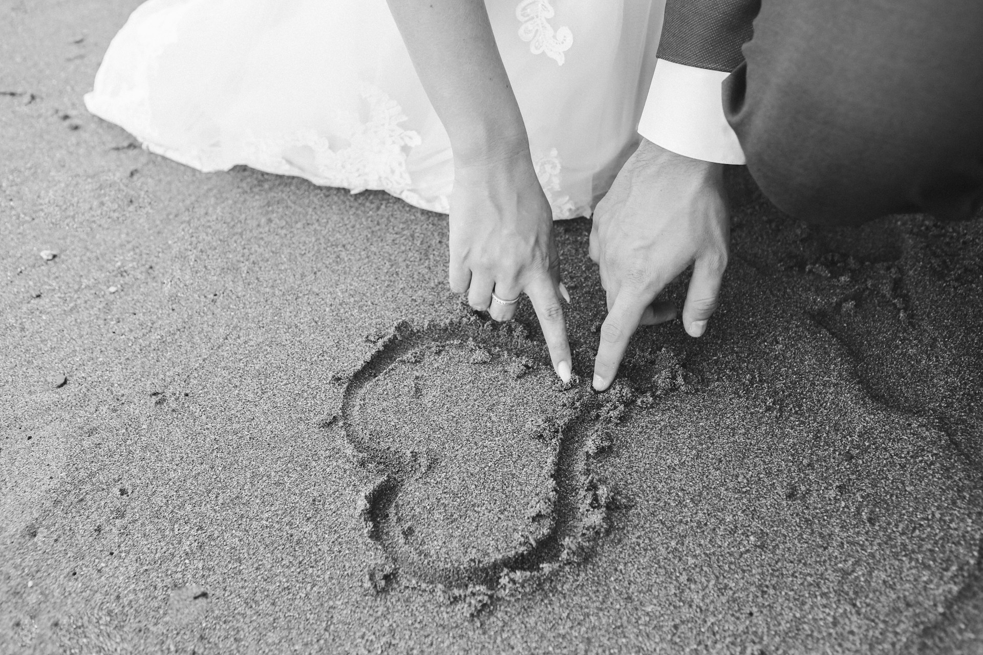 Photo en niveaux de gris d'un couple dessinant un cœur sur le sable | Source : Unsplash