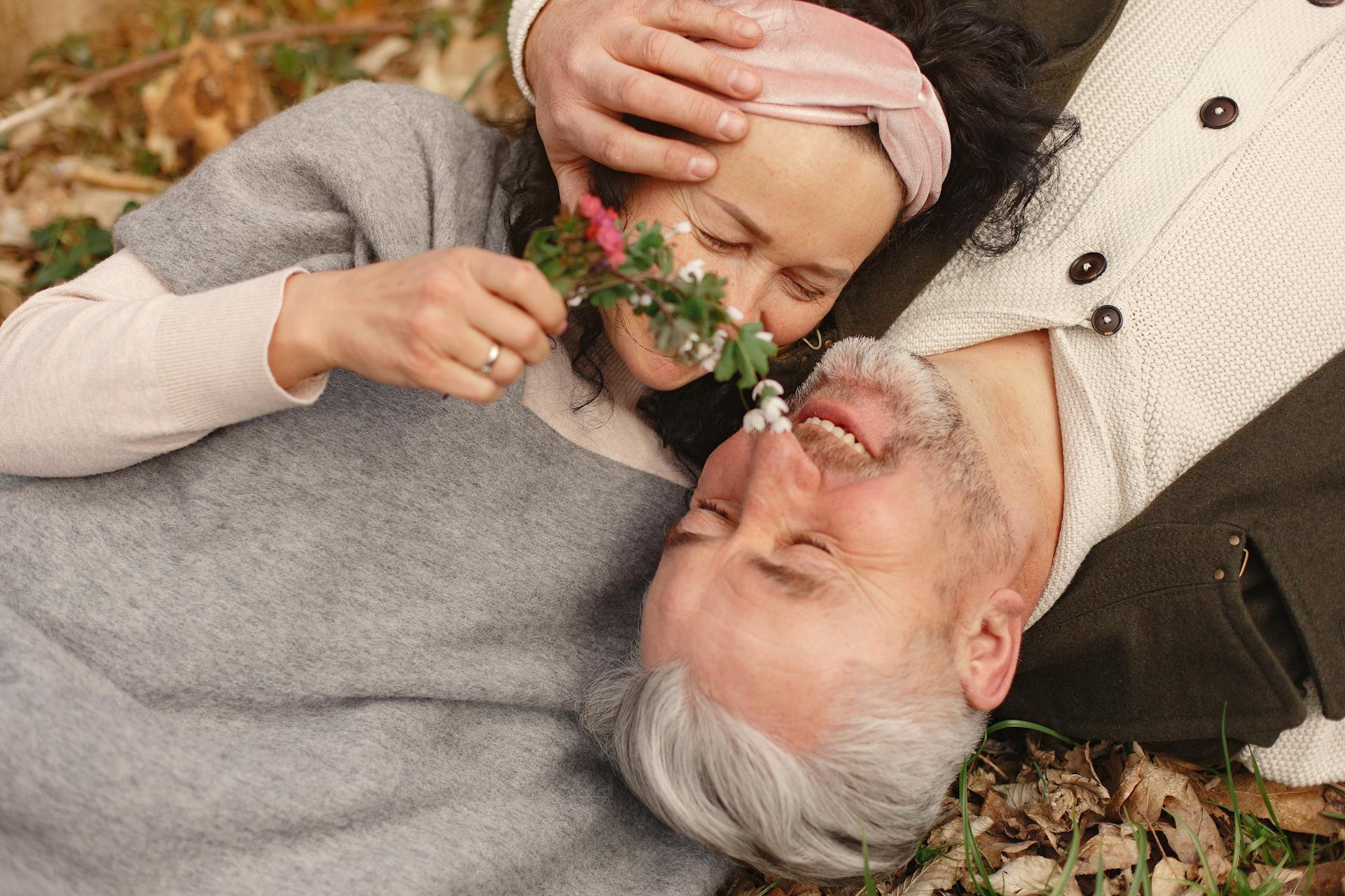 Un couple de seniors se câline en s'allongeant sur un bouquet de feuilles mortes | Source : Pexels