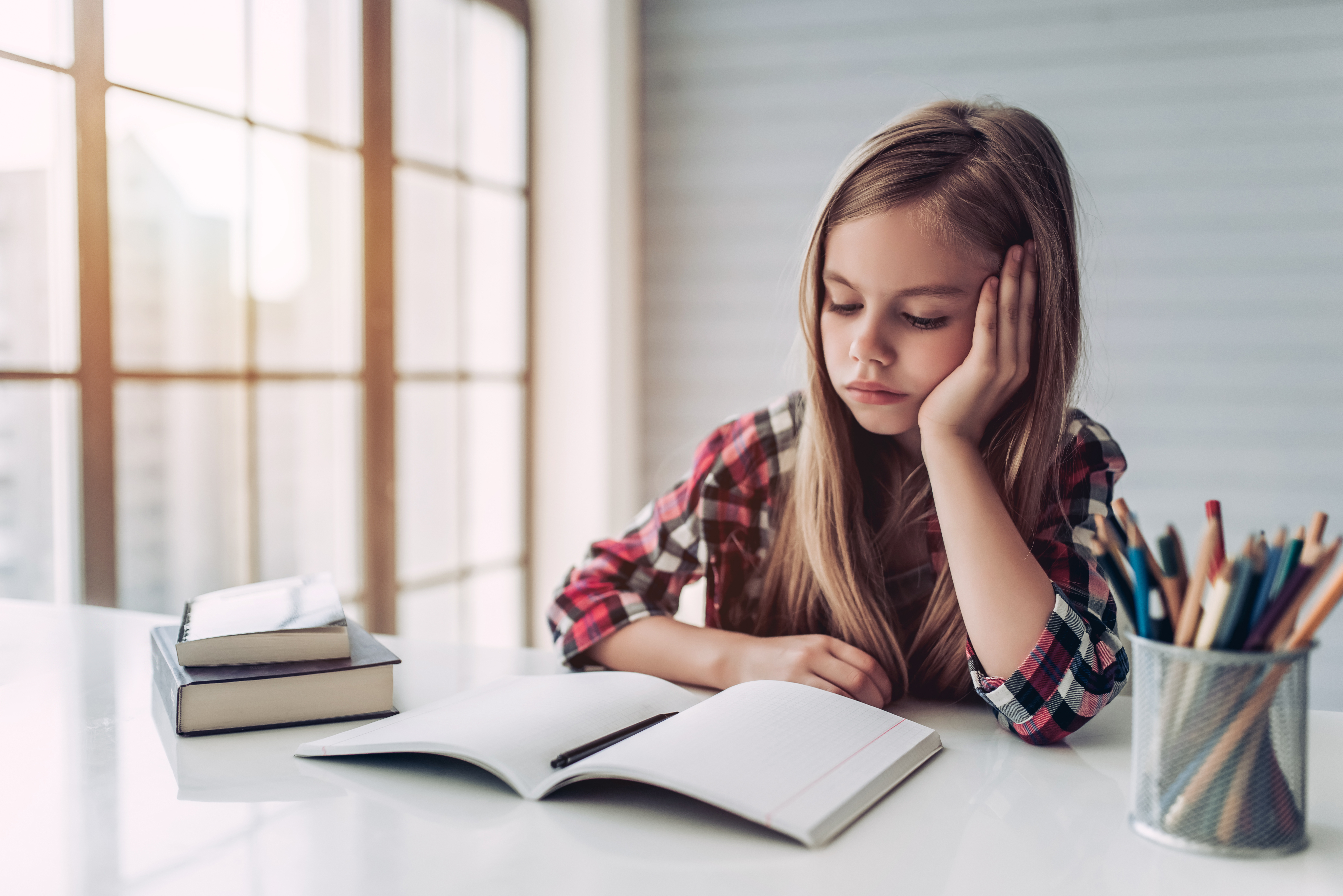 Une jeune fille triste fixant un livre sur son bureau | Source : Shutterstock