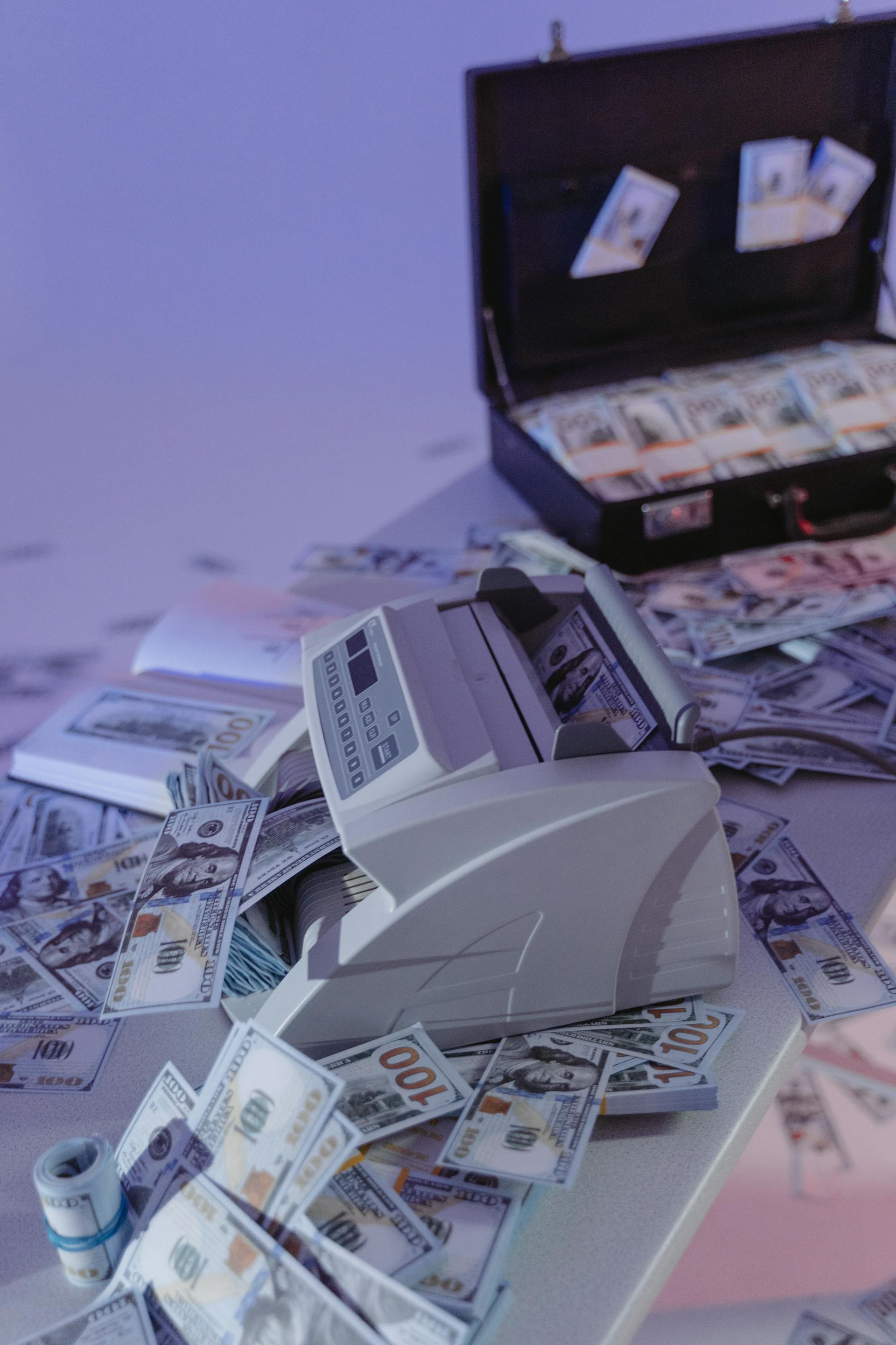 A money counting machine and a suitcase hidden with cash | Source: Pexels