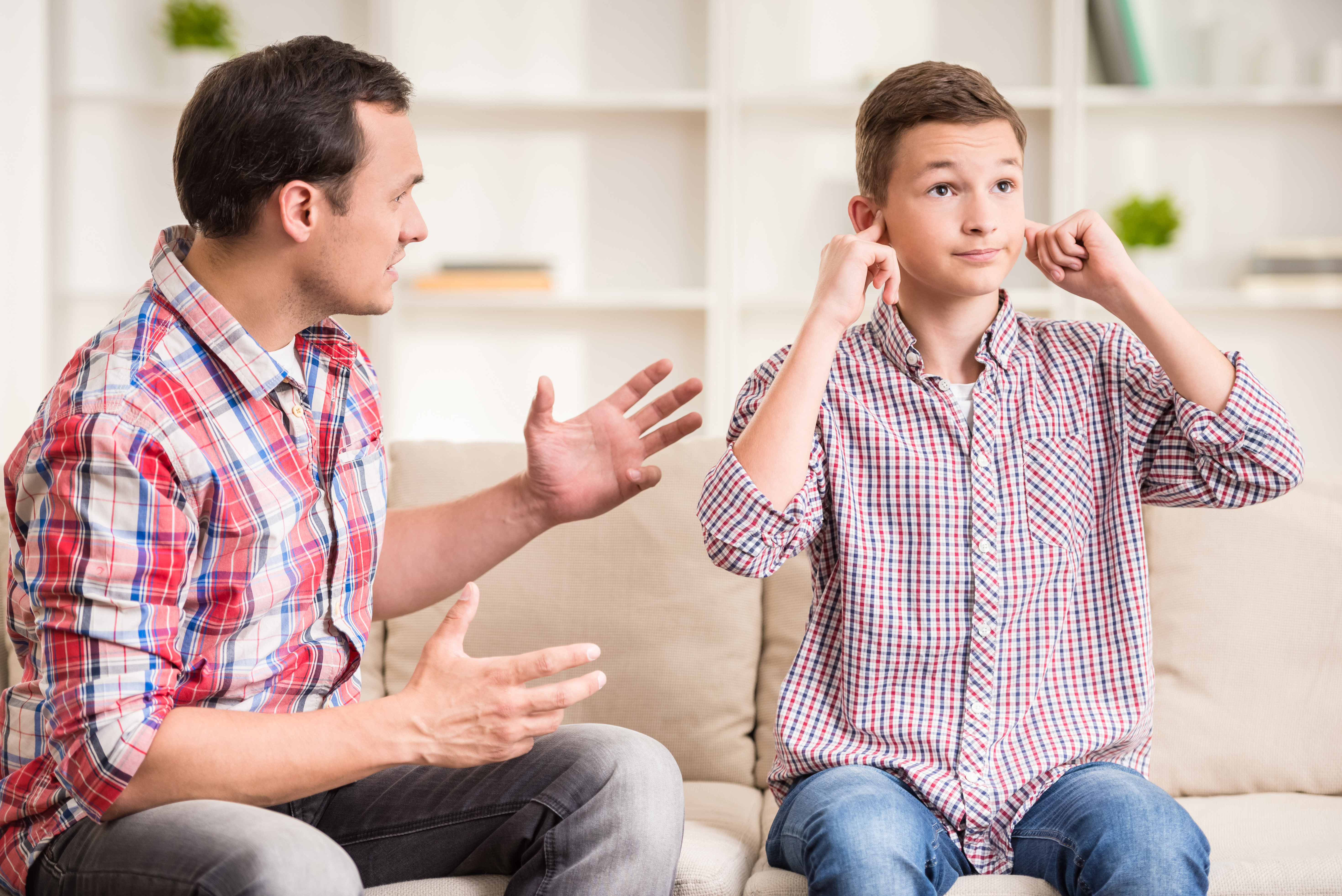 Fils se bouchant les oreilles pendant que son père lui parle| Source : Shutterstock