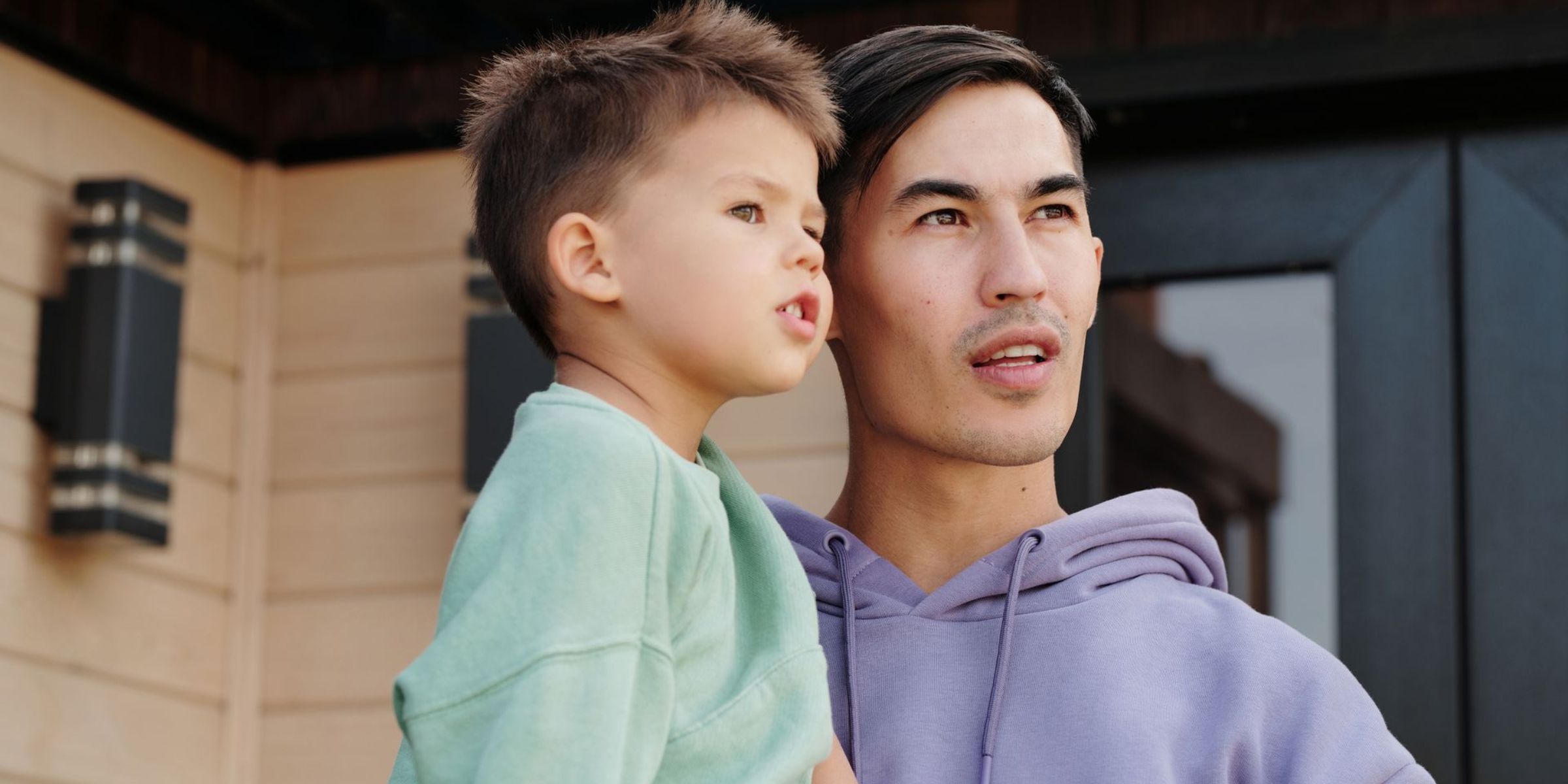 Un père tenant son jeune fils dans les bras devant chez eux | Source : Pexels