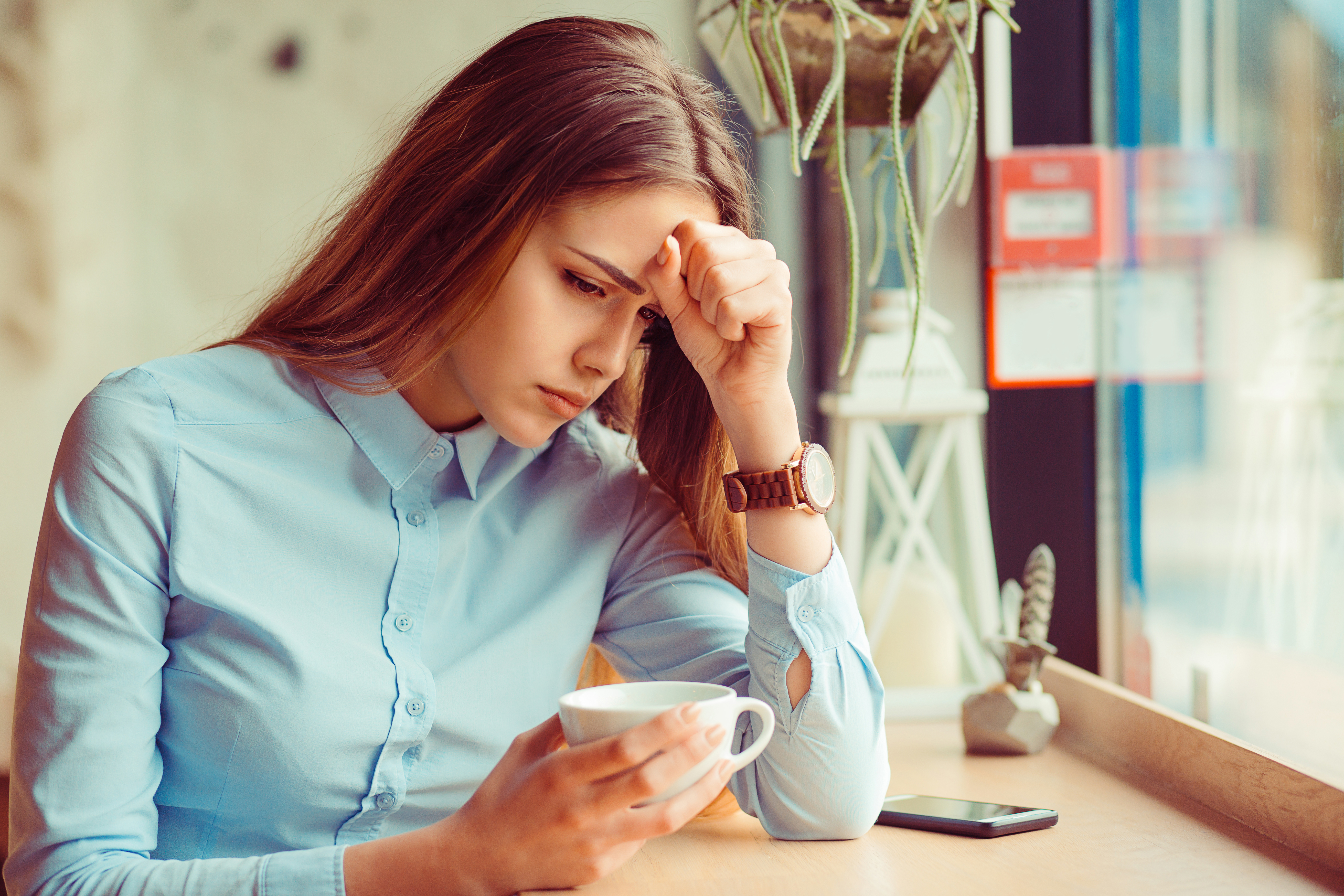 Jeune femme stressée avec une tasse de café, assise dans un café | Source : Shutterstock