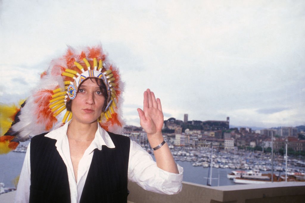 Portrait de Corine Marienneau, chanteuse et bassiste du groupe de rock français Téléphone, portant une coiffe indienne avec des plumes devant un port de pêche, circa 1980. | Photo : Getty Images