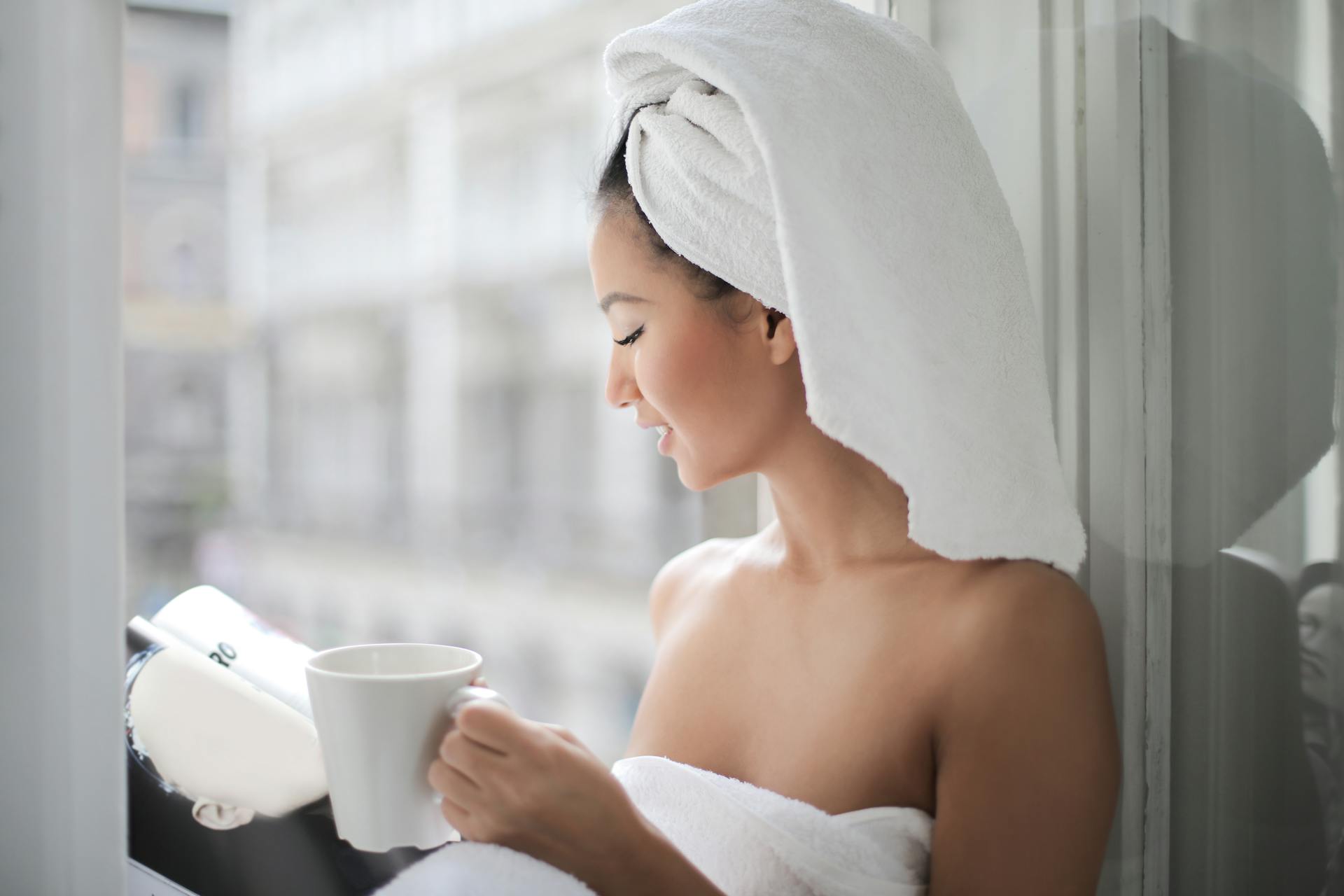 Une femme lisant un magazine et tenant une tasse près d'une fenêtre en verre | Source : Pexels