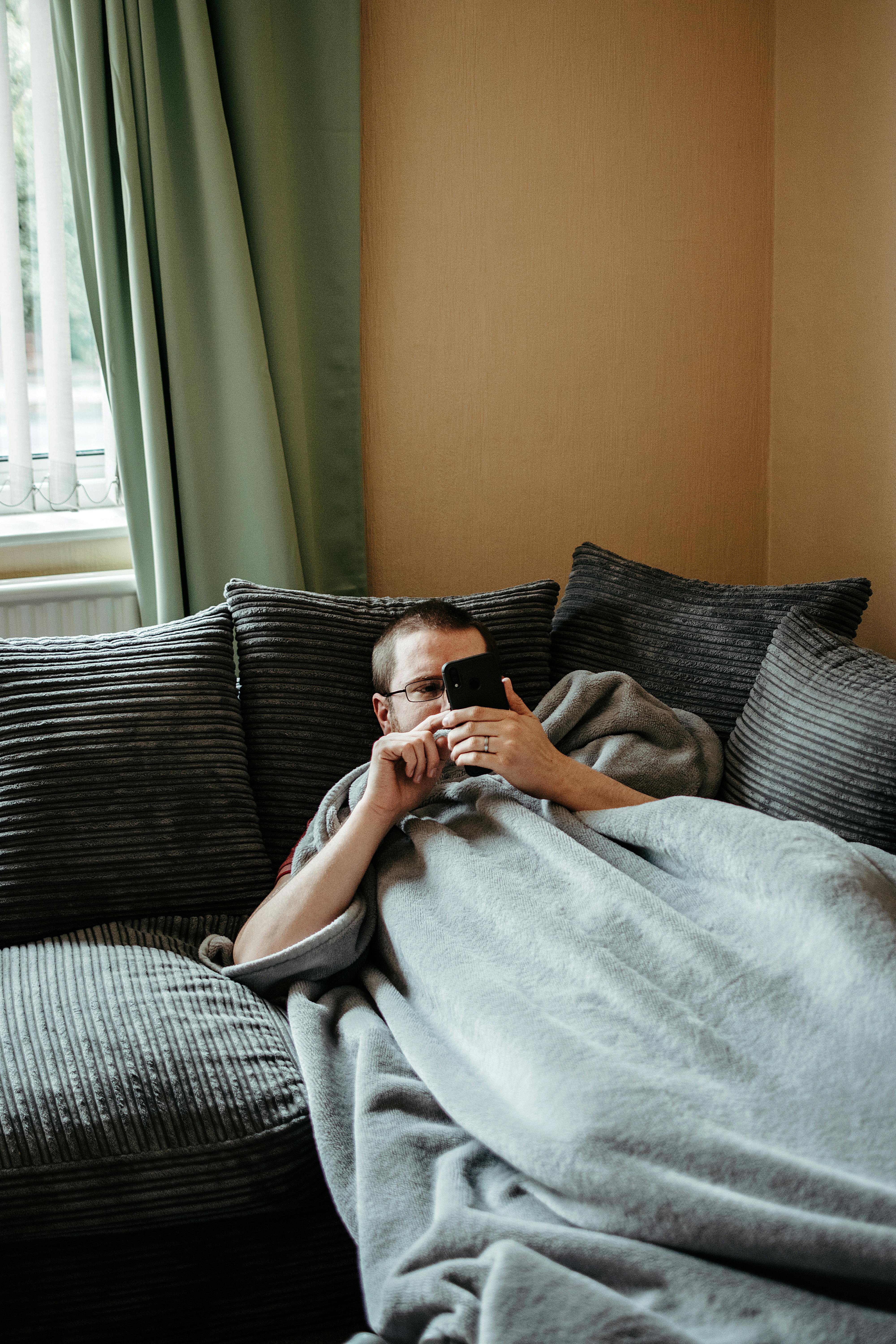Un homme paresse sur un canapé tout en utilisant son téléphone | Source : Pexels