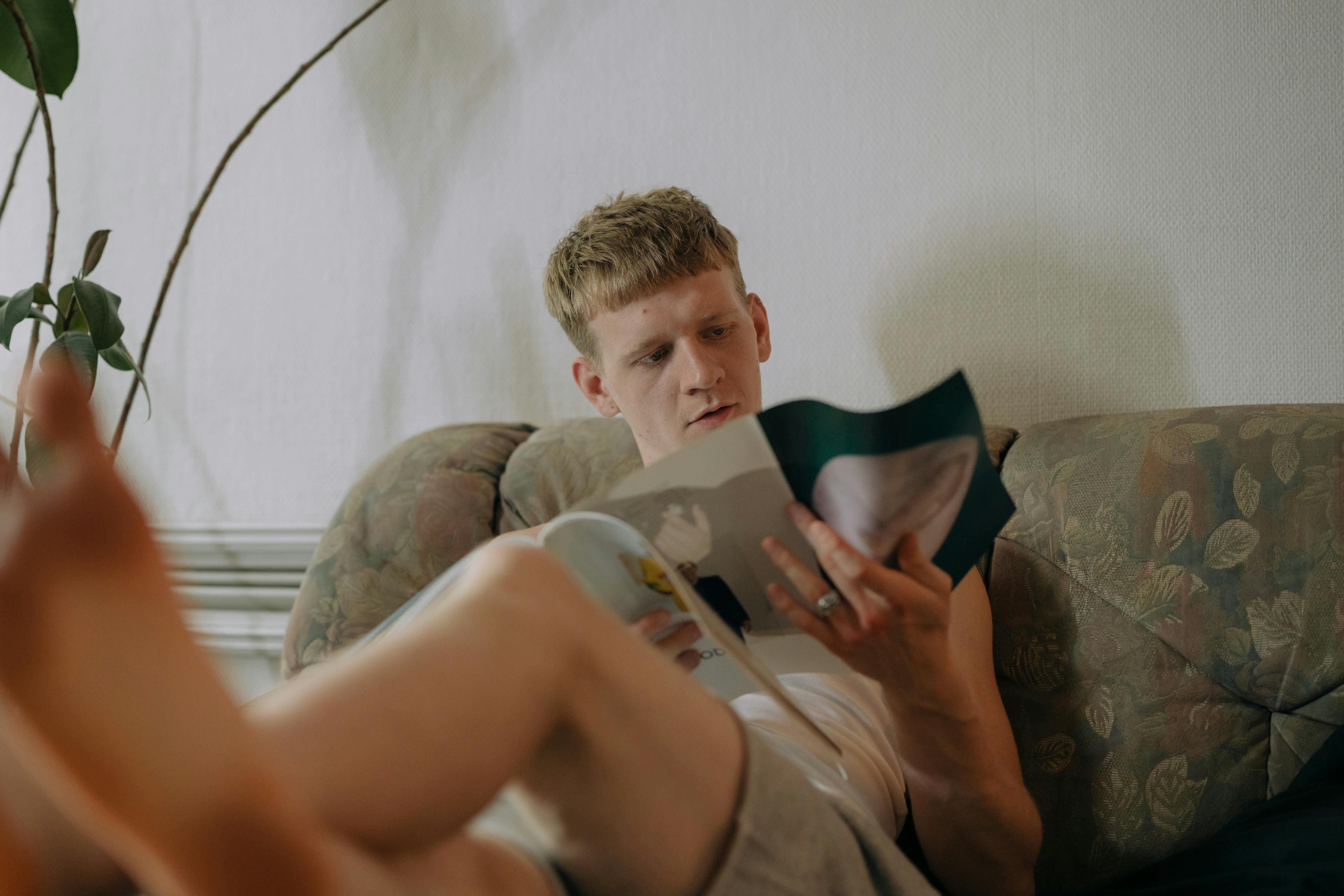 Un homme assis sur le canapé en train de lire un magazine | Source : Pexels