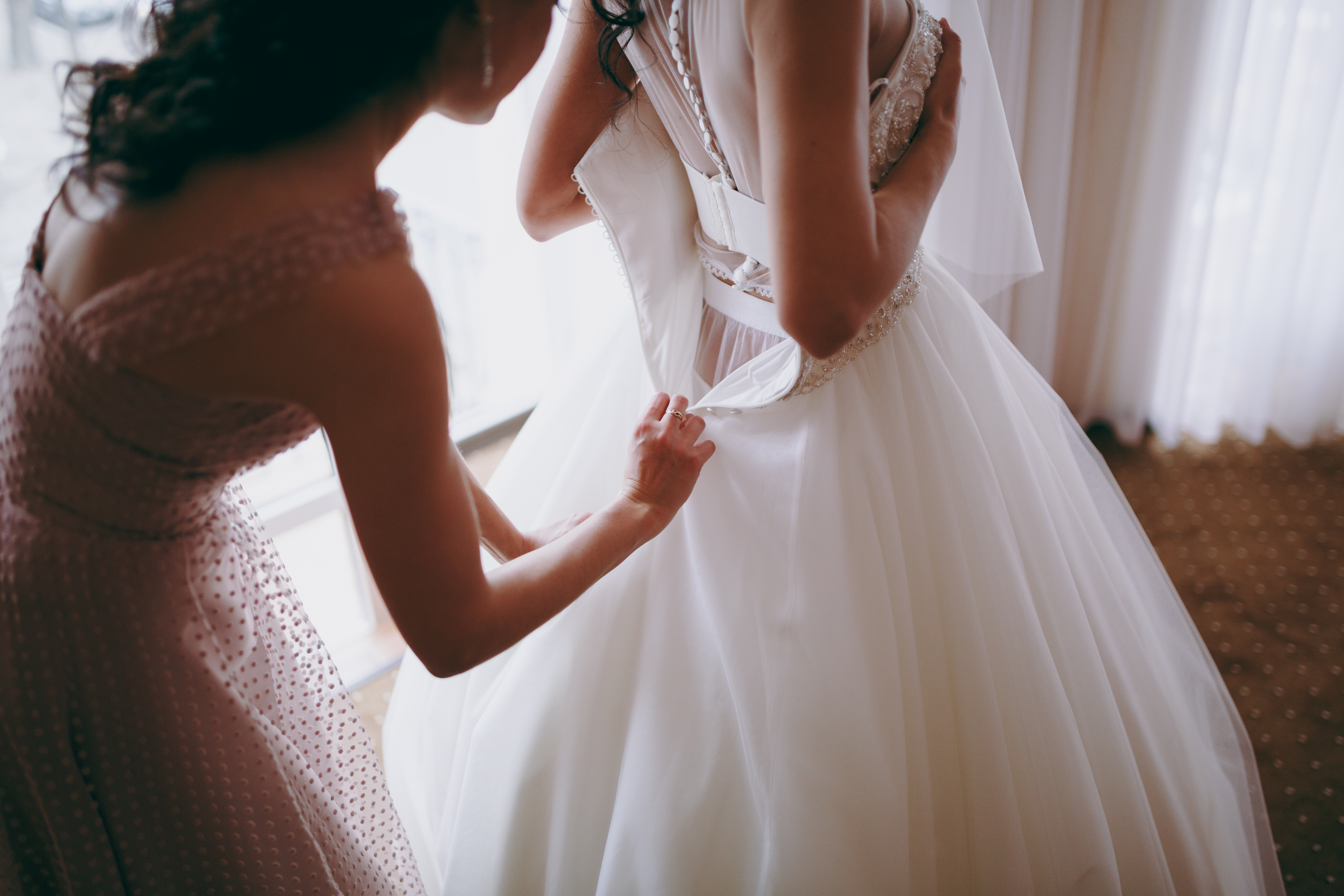 Une femme aidant une mariée à enfiler sa robe de mariée | Source : Shutterstock