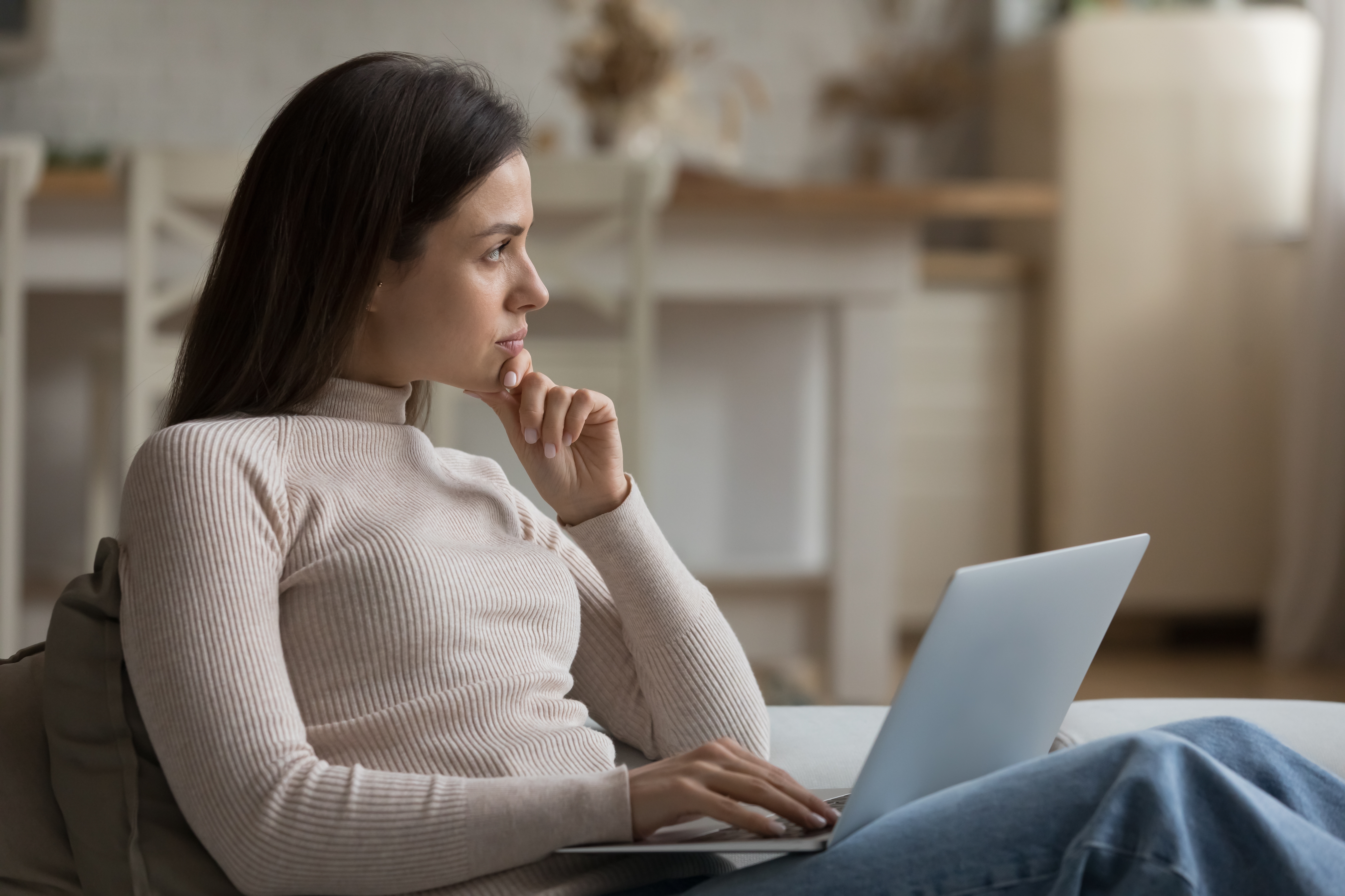 Une jeune femme pensive qui regarde au loin tout en utilisant son ordinateur portable | Source : Shutterstock