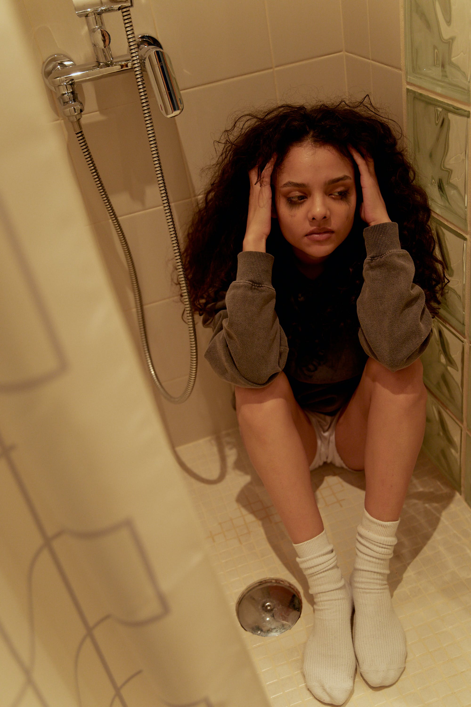Une jeune femme bouleversée qui pleure en s'asseyant sur le sol d'une douche | Source : Pexels
