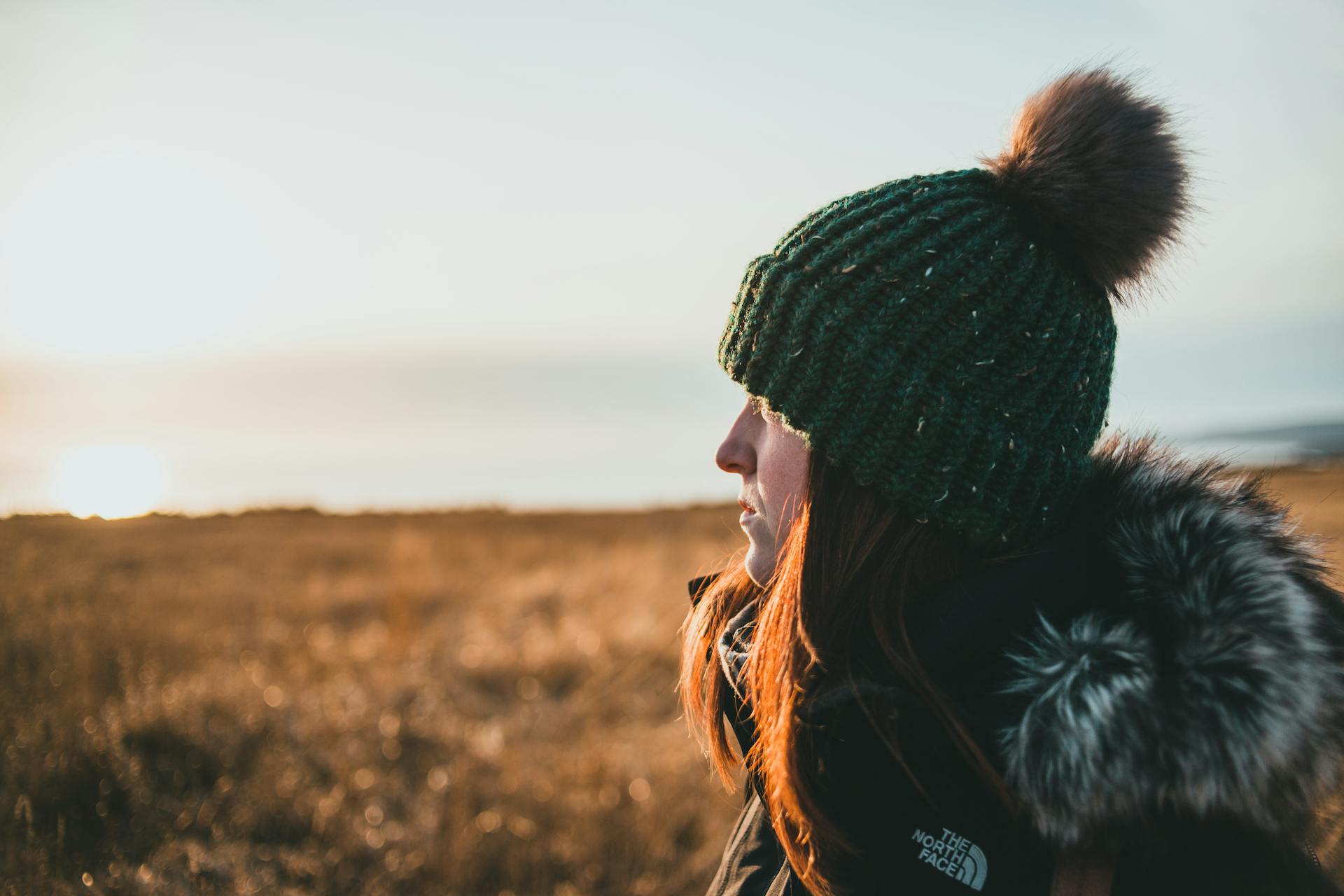 Gros plan sur une femme admirant la nature sur un bord de mer herbeux au coucher du soleil | Source : Pexels