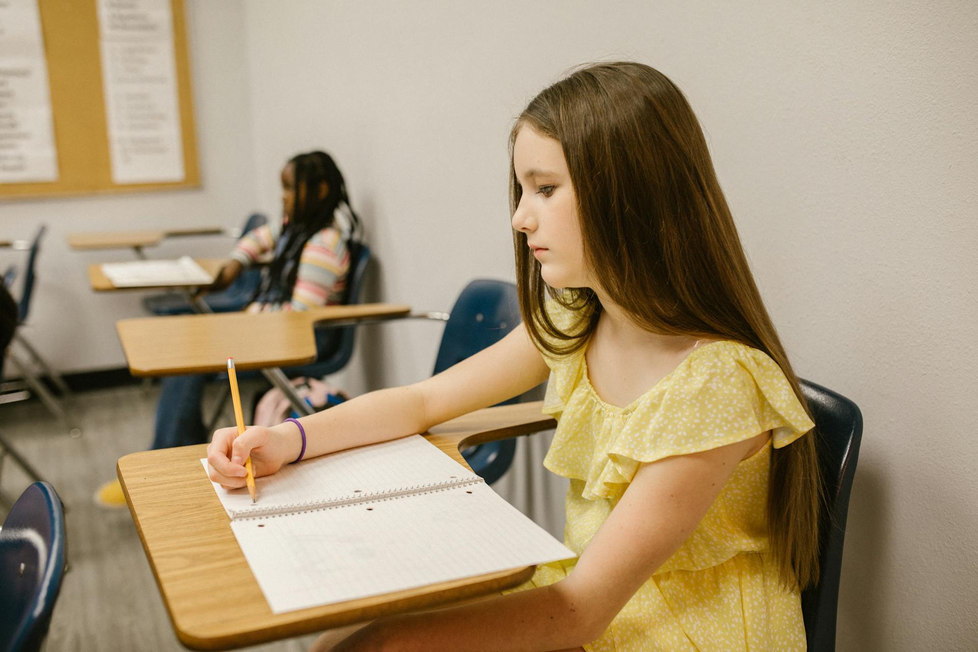 Une fille en détresse assise dans sa classe et écrivant sur son cahier | Source : Pexels