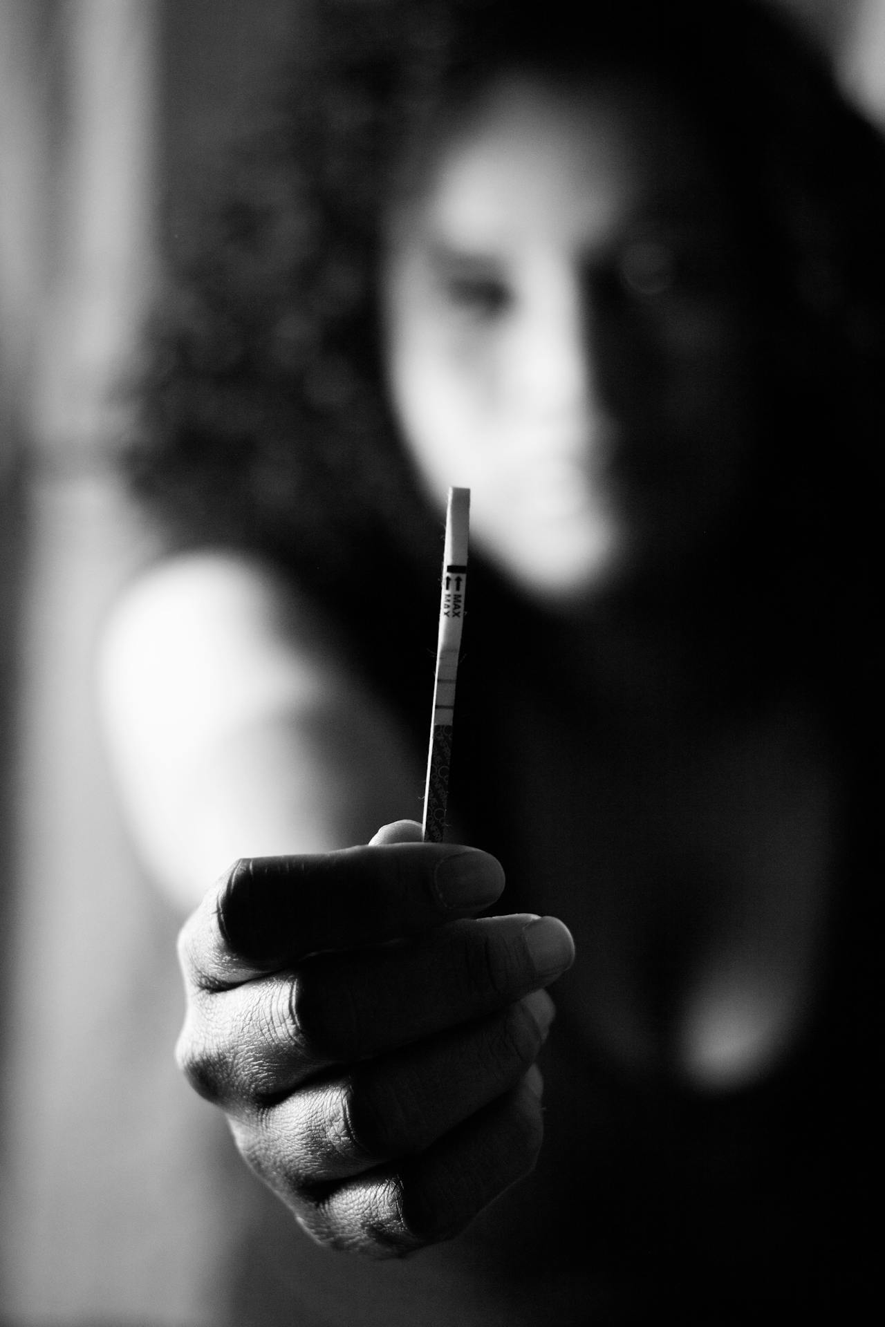 Photo en niveaux de gris d'une femme tenant un test de grossesse au point | Source : Pexels