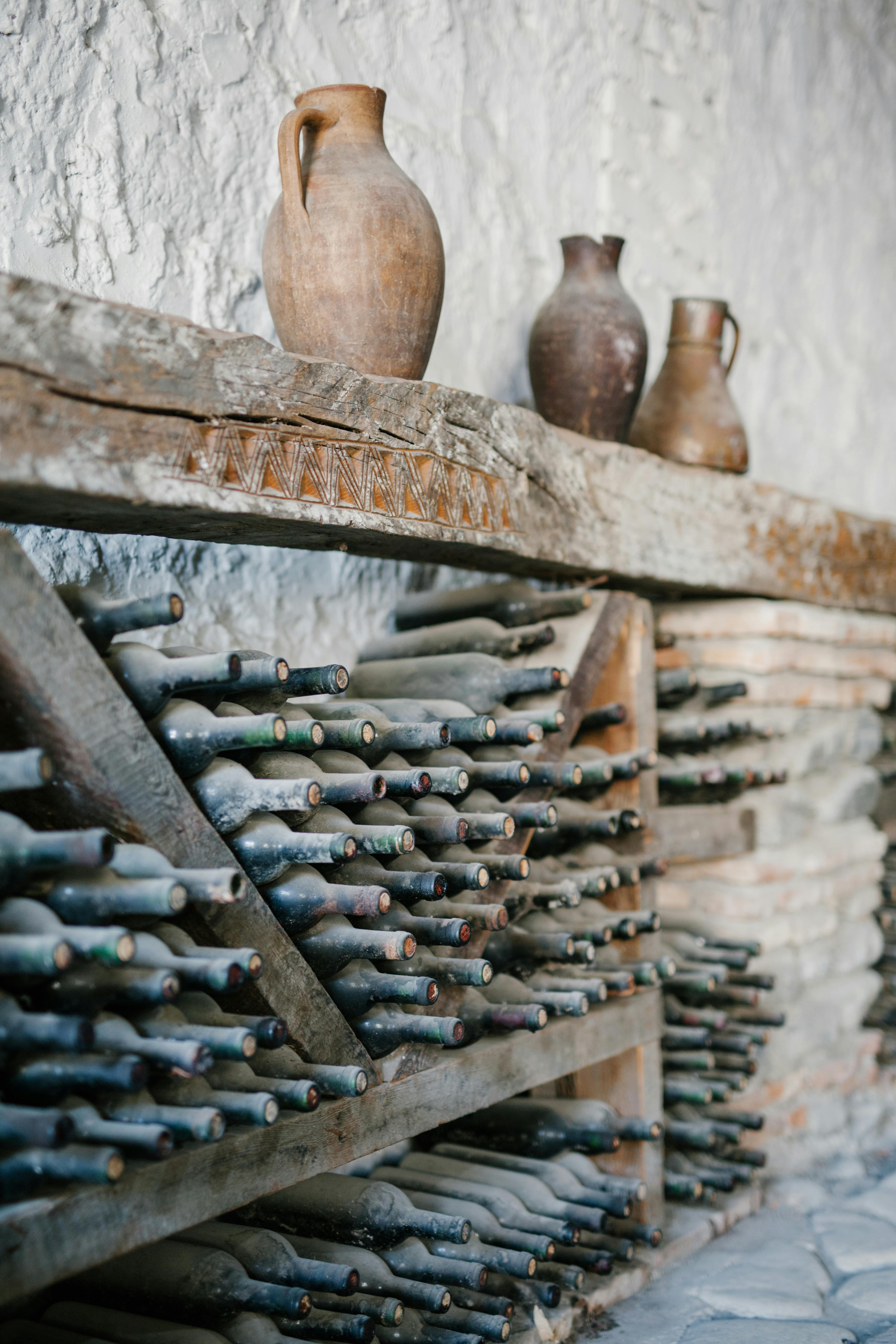 Étagères en bois avec des bouteilles de vin en verre poussiéreuses | Source : Pexels
