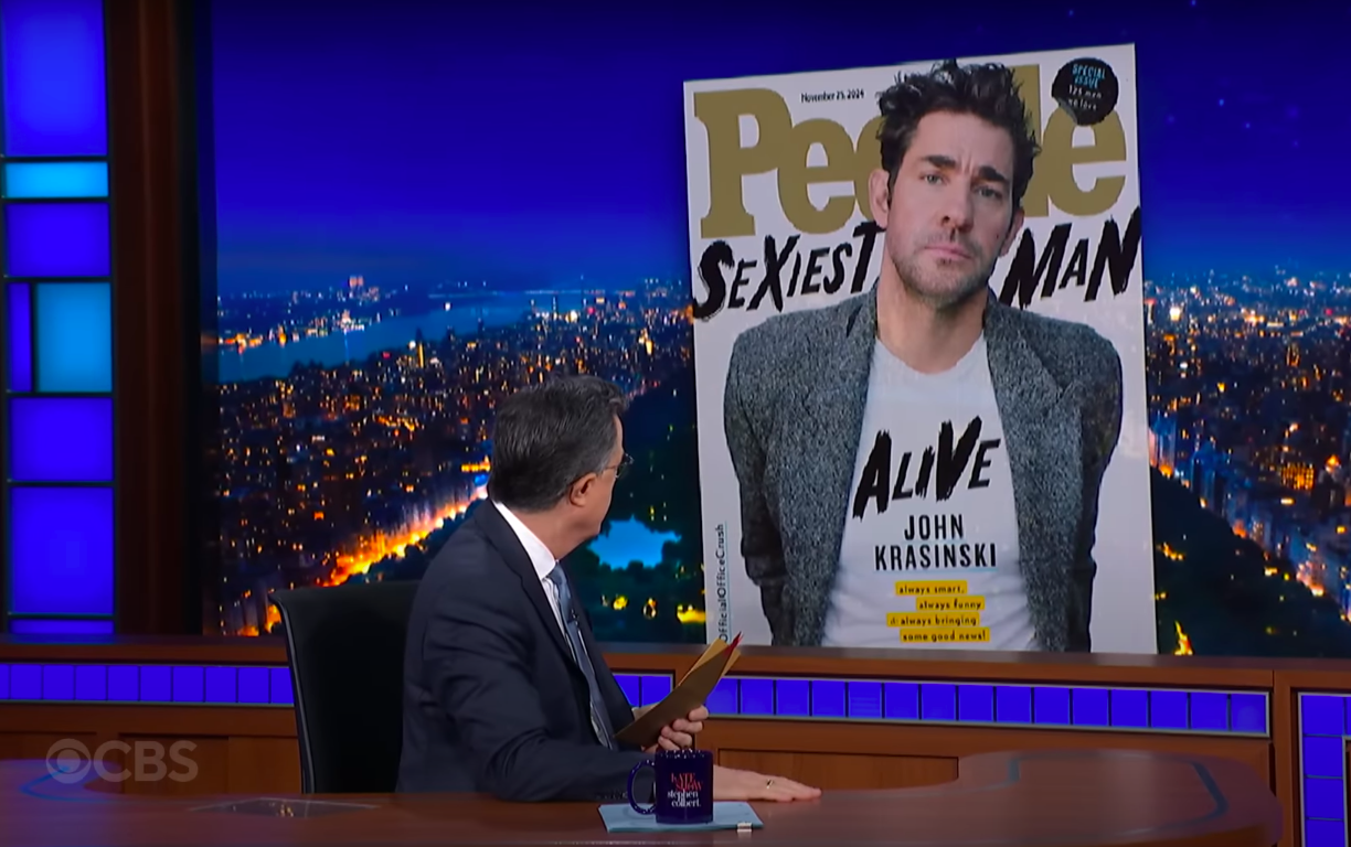 Stephen Colbert regardant la photo de John Krasinski en couverture du magazine People lors d'un épisode du "The Late Show with Stephen Colbert", posté le 13 novembre 2024 | Source : YouTube/The Late Show with Stephen Colbert