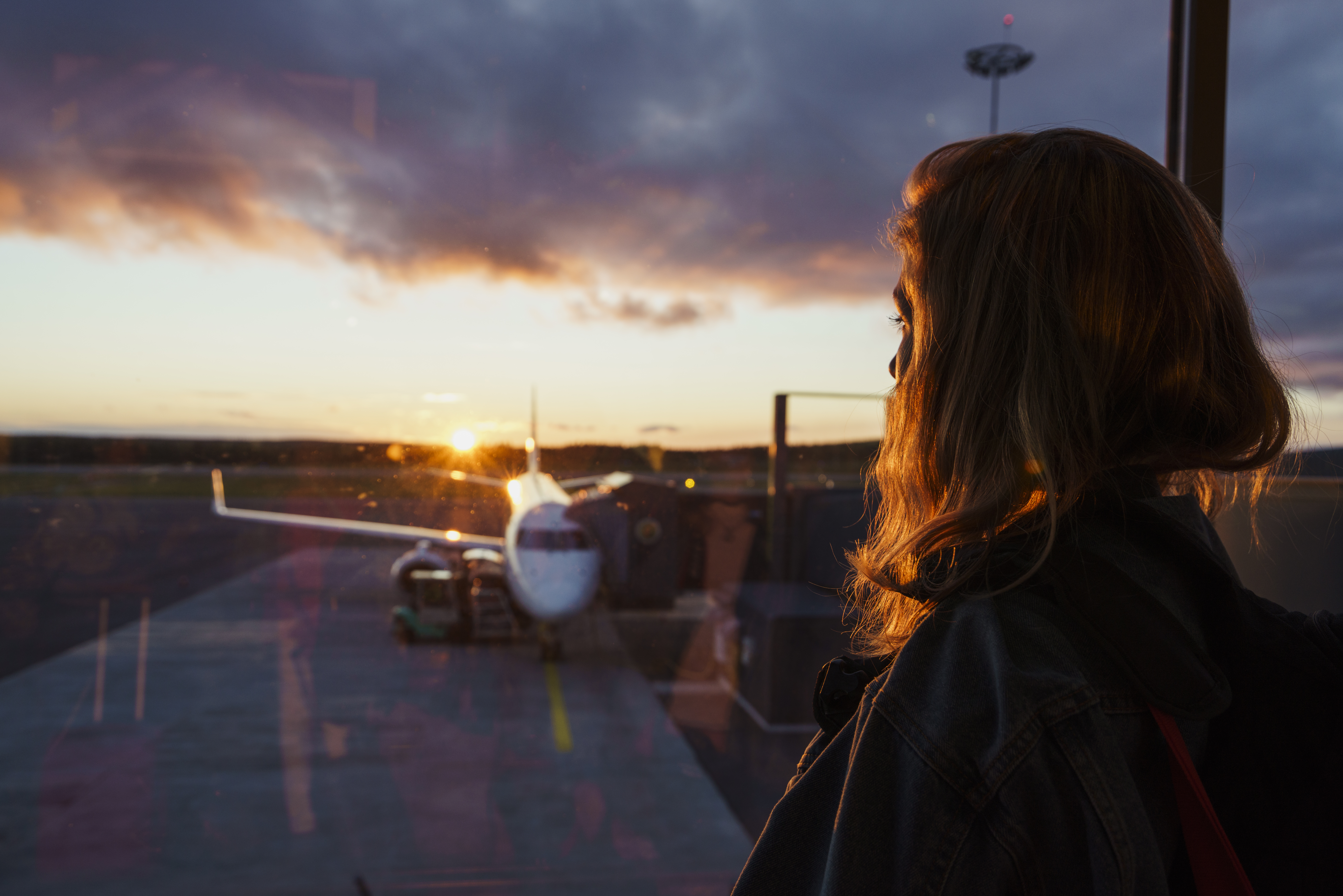 Jeune femme regardant par le hublot d'un avion à l'aéroport au coucher du soleil | Source : Getty Images