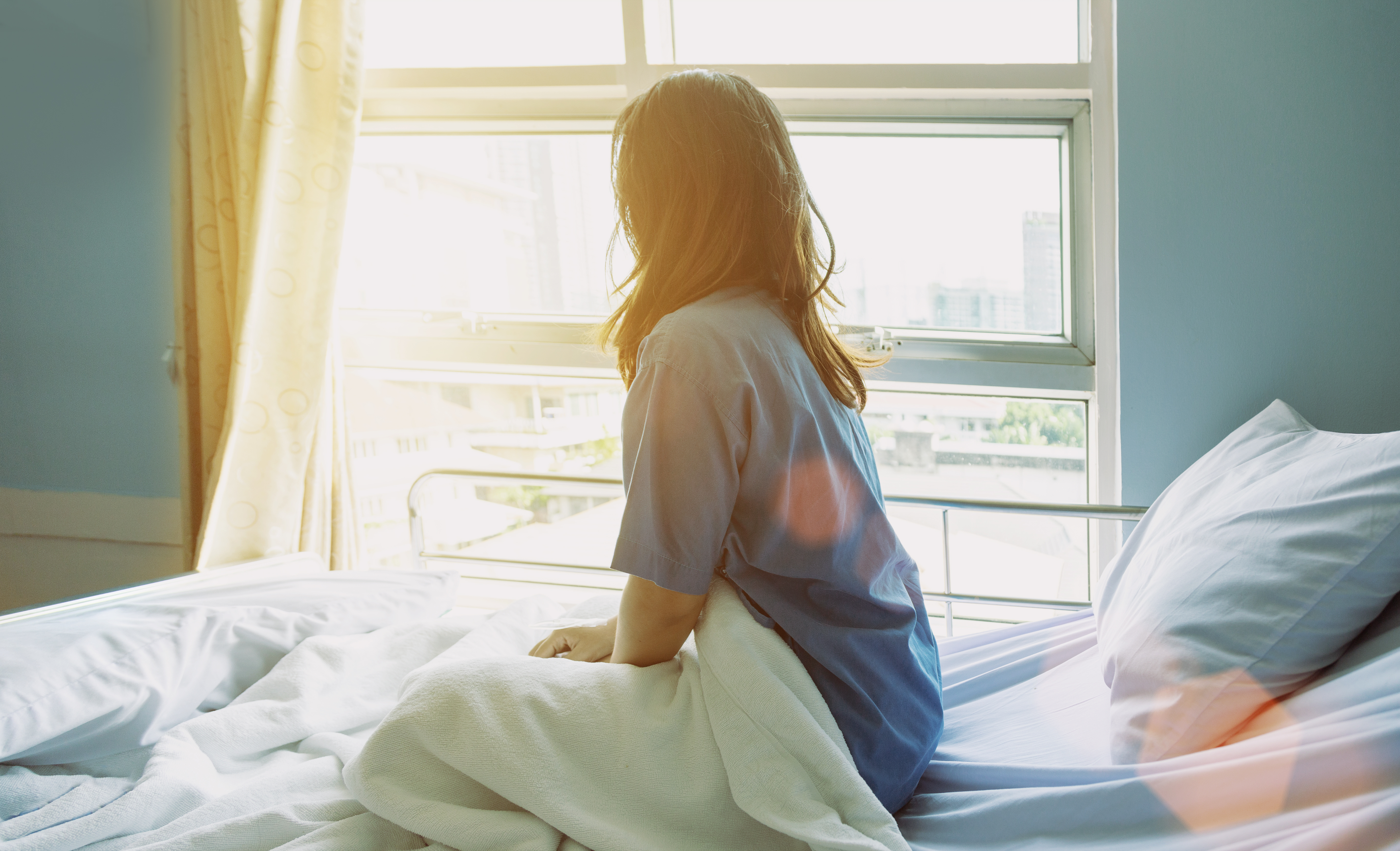 Une femme regarde par la fenêtre alors qu'elle est assise sur un lit d'hôpital | Source : Shutterstock