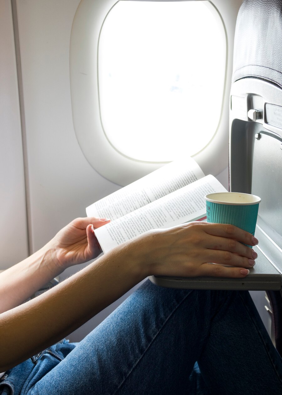 Une femme avec un livre et un café dans un siège de fenêtre | Source : Freepik