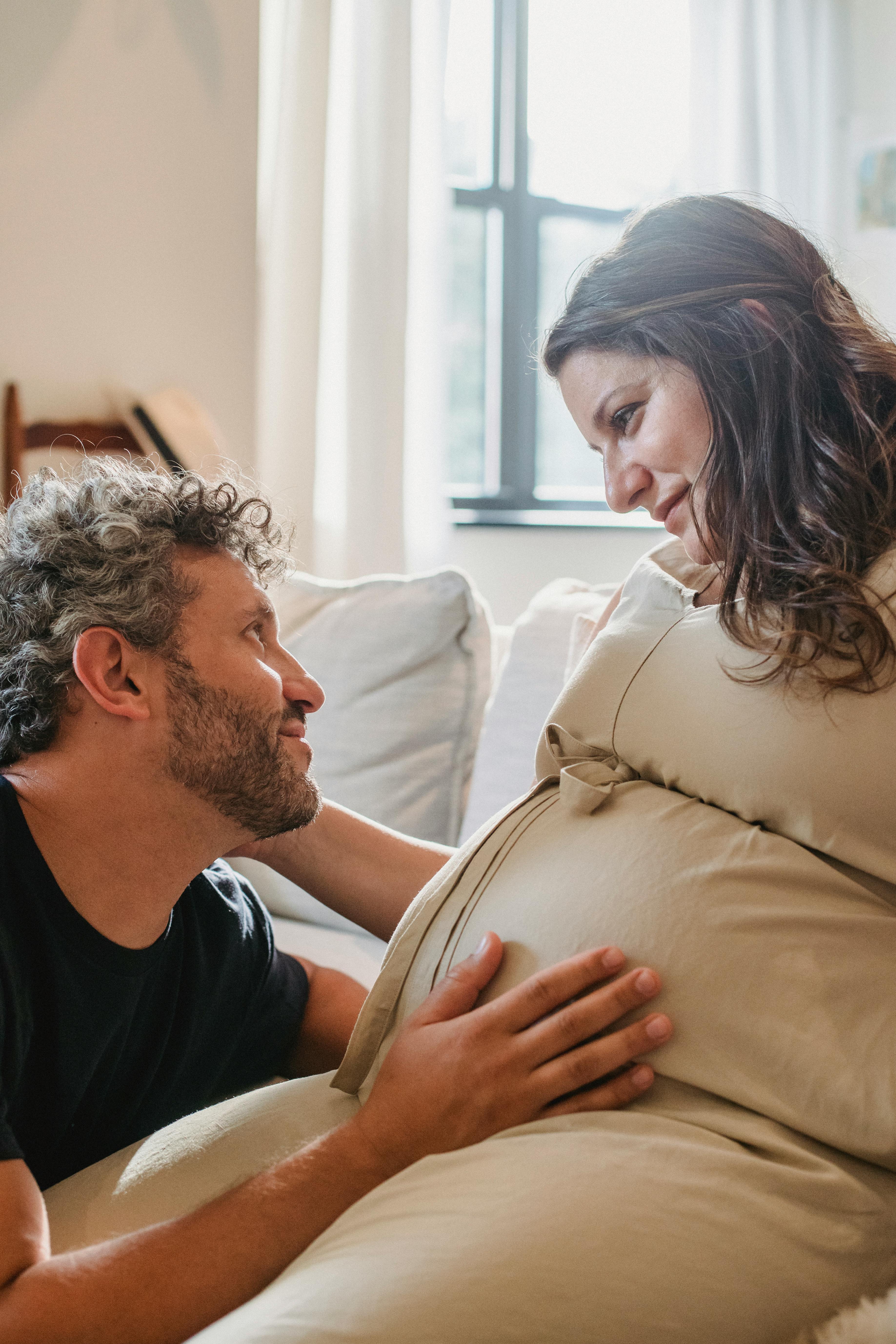 Homme touchant le ventre de sa femme enceinte alors qu'ils se regardent fixement | Source : Pexels