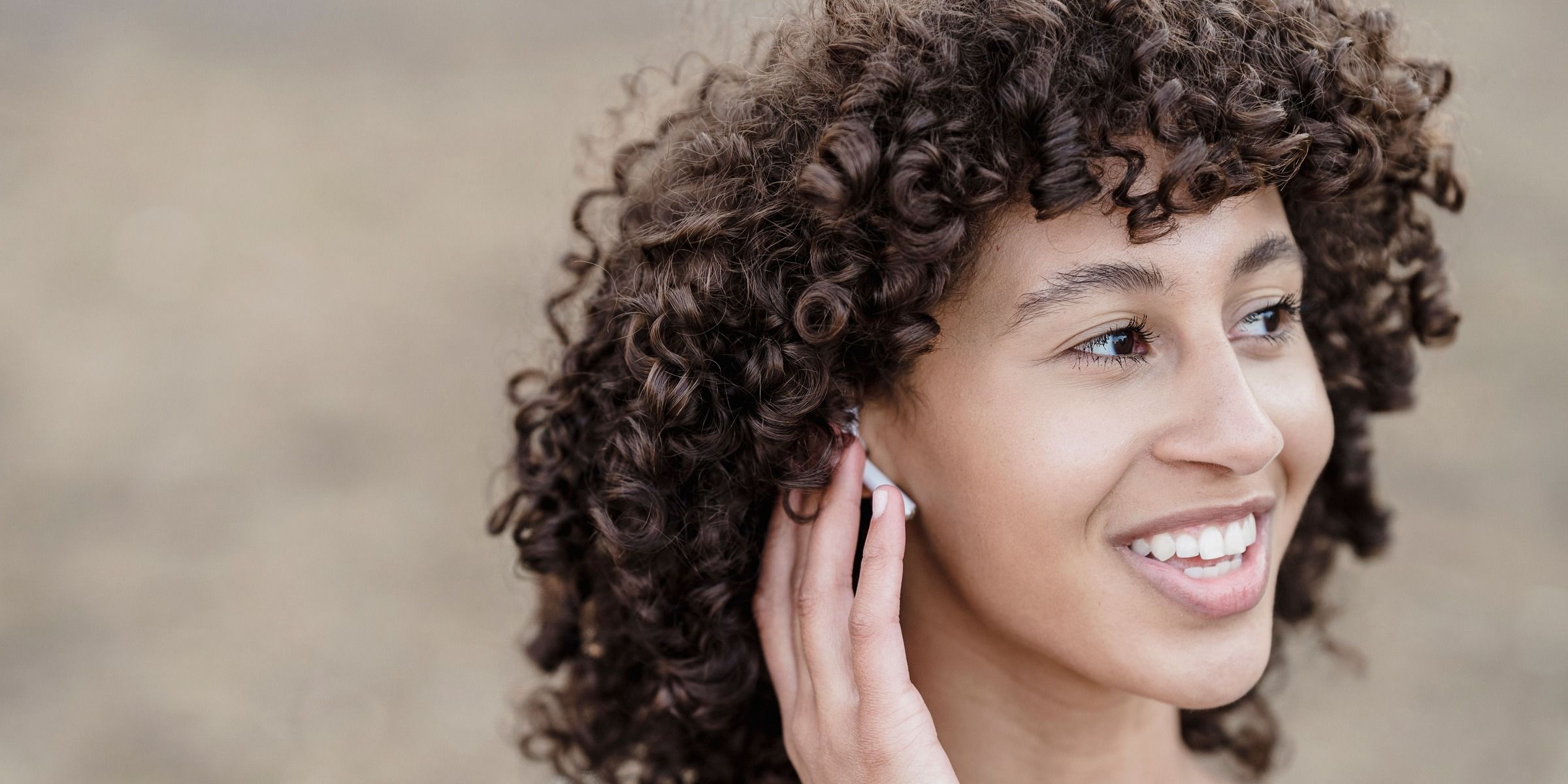 Une jeune femme souriante qui se tient l'oreille | Source : Pexels