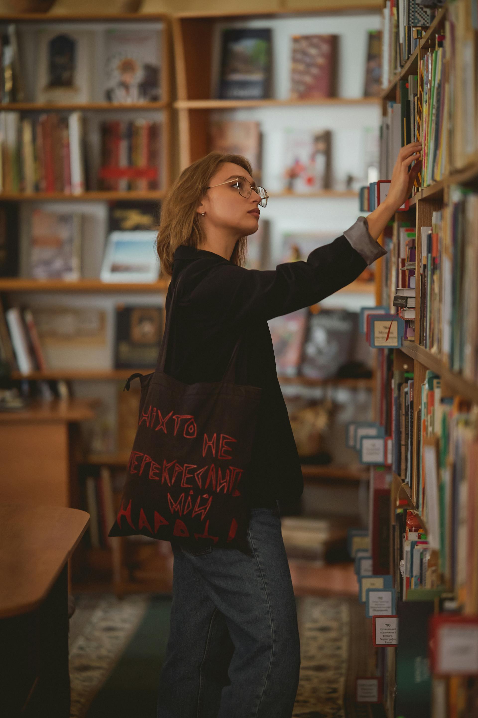 Une jeune femme prenant un livre sur une étagère | Source : Pexels