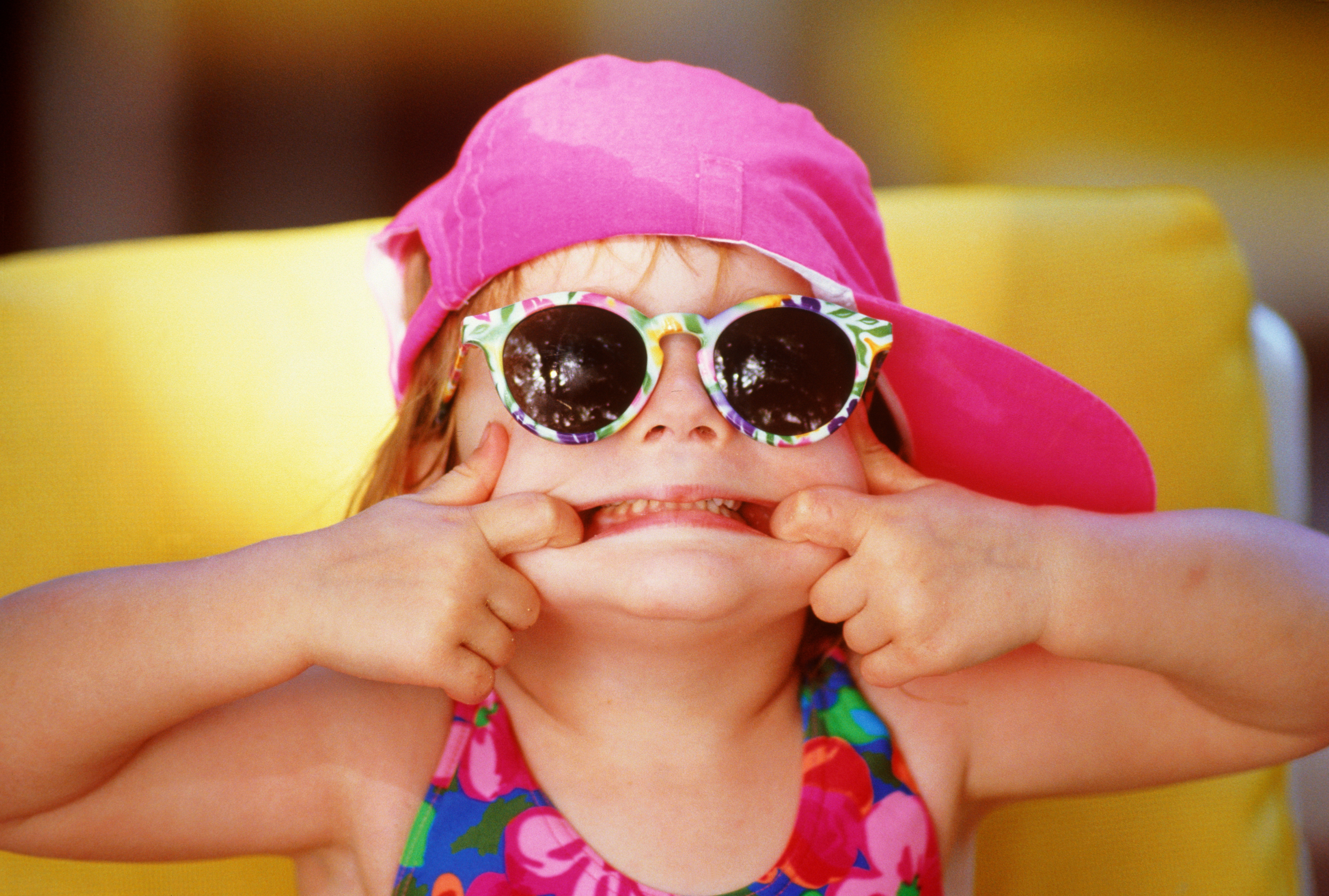 Petite fille en maillot de bain, casquette et lunettes de soleil, tirant le visage, gros plan | Source : Getty Images