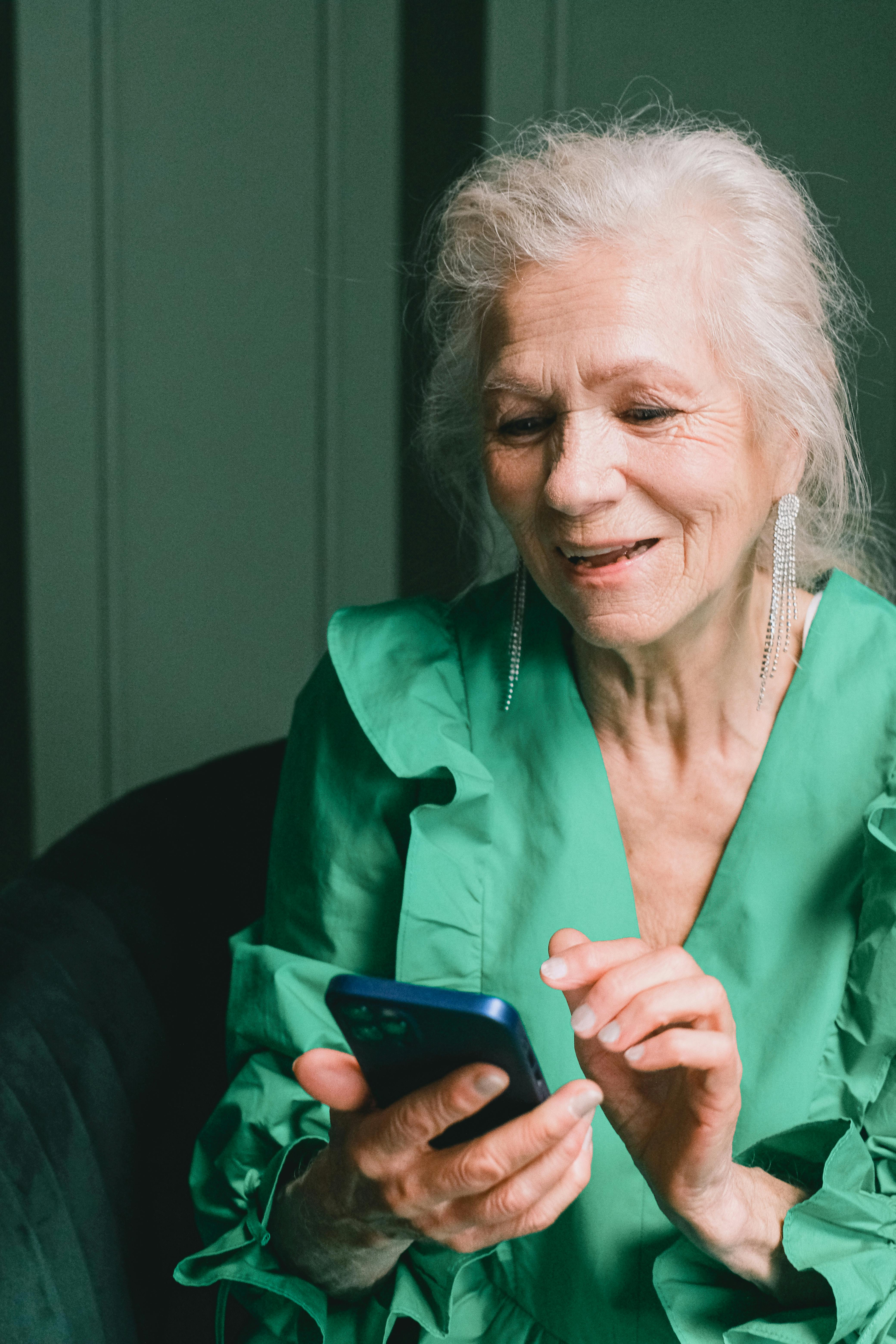 Une femme âgée qui sourit tout en utilisant un téléphone | Source : Pexels