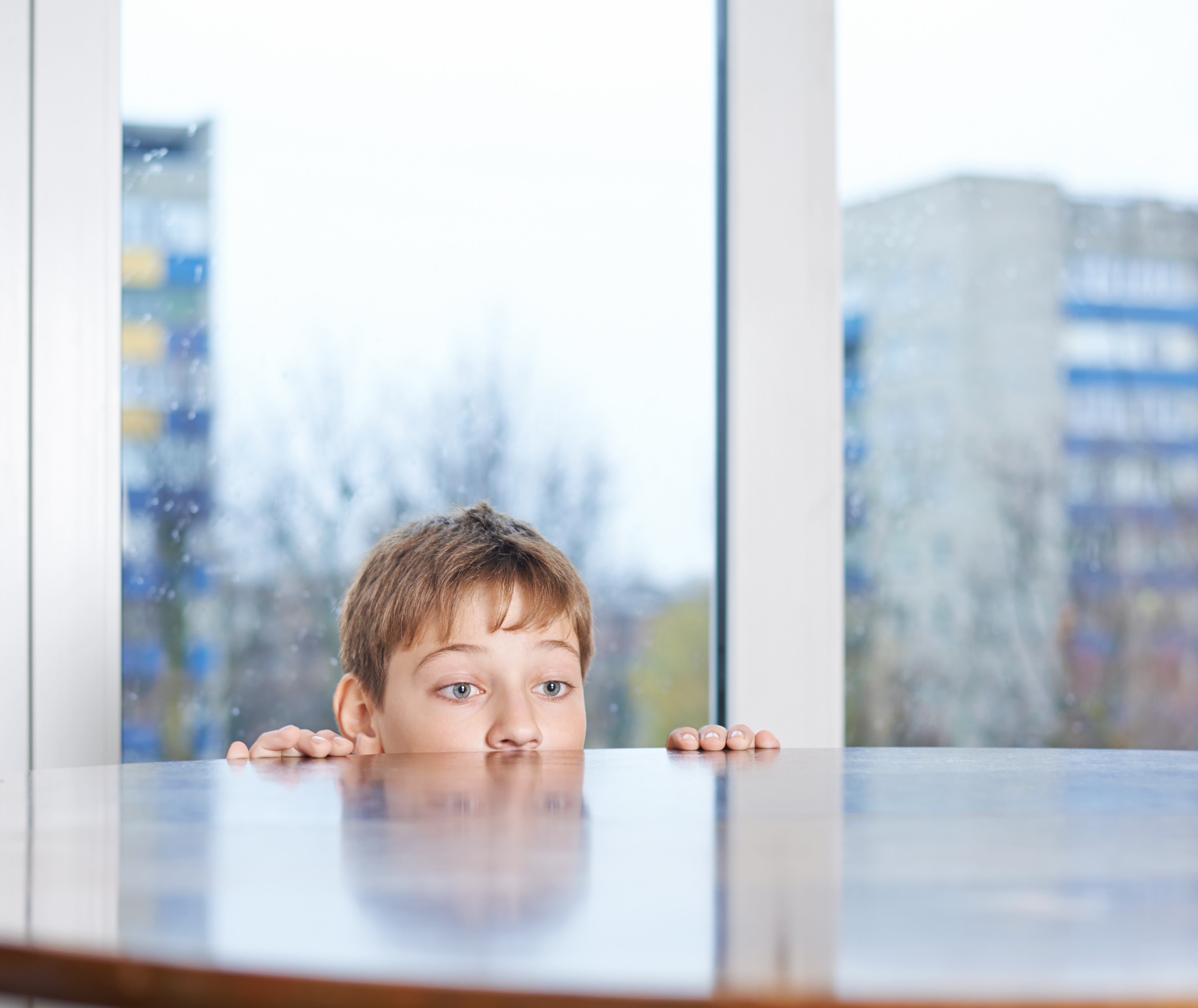 Un jeune garçon jetant un coup d'œil derrière une table en bois | Source : Shutterstock