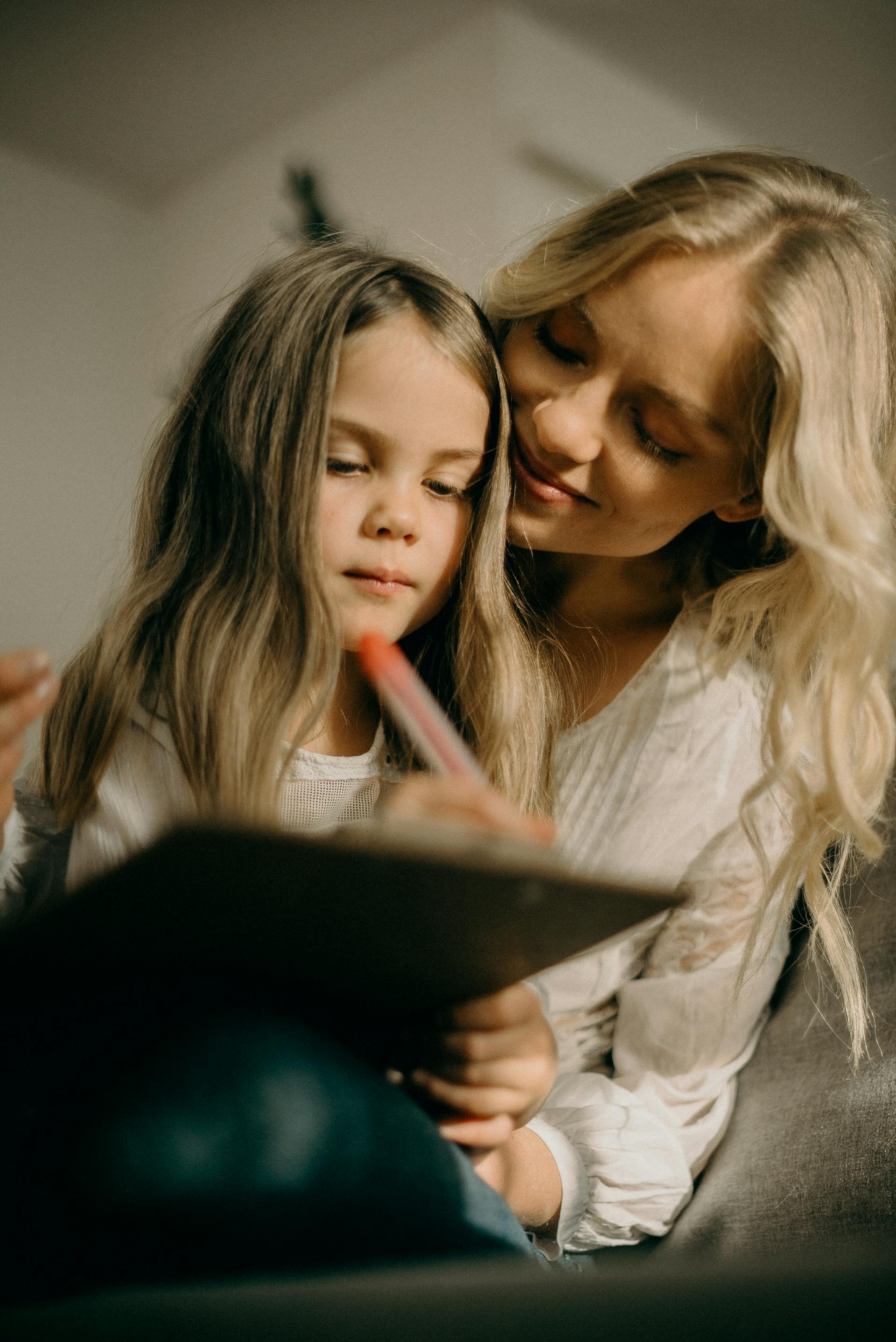 Une petite fille dessine quelque chose sur un papier tout en étant assise à côté d'une femme blonde | Source : Pexels