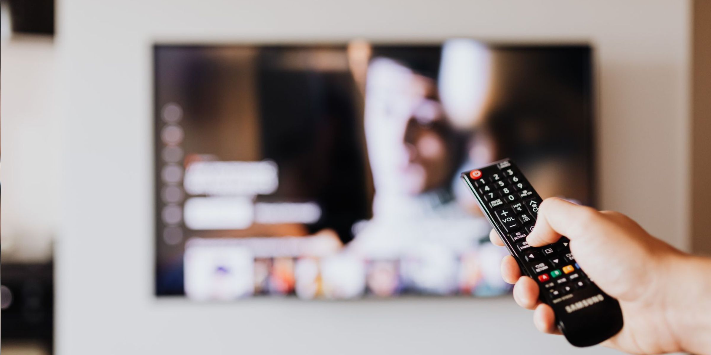 Une personne qui utilise une télécommande de télé, avec un écran de télé flou en arrière-plan | Source : Pexels