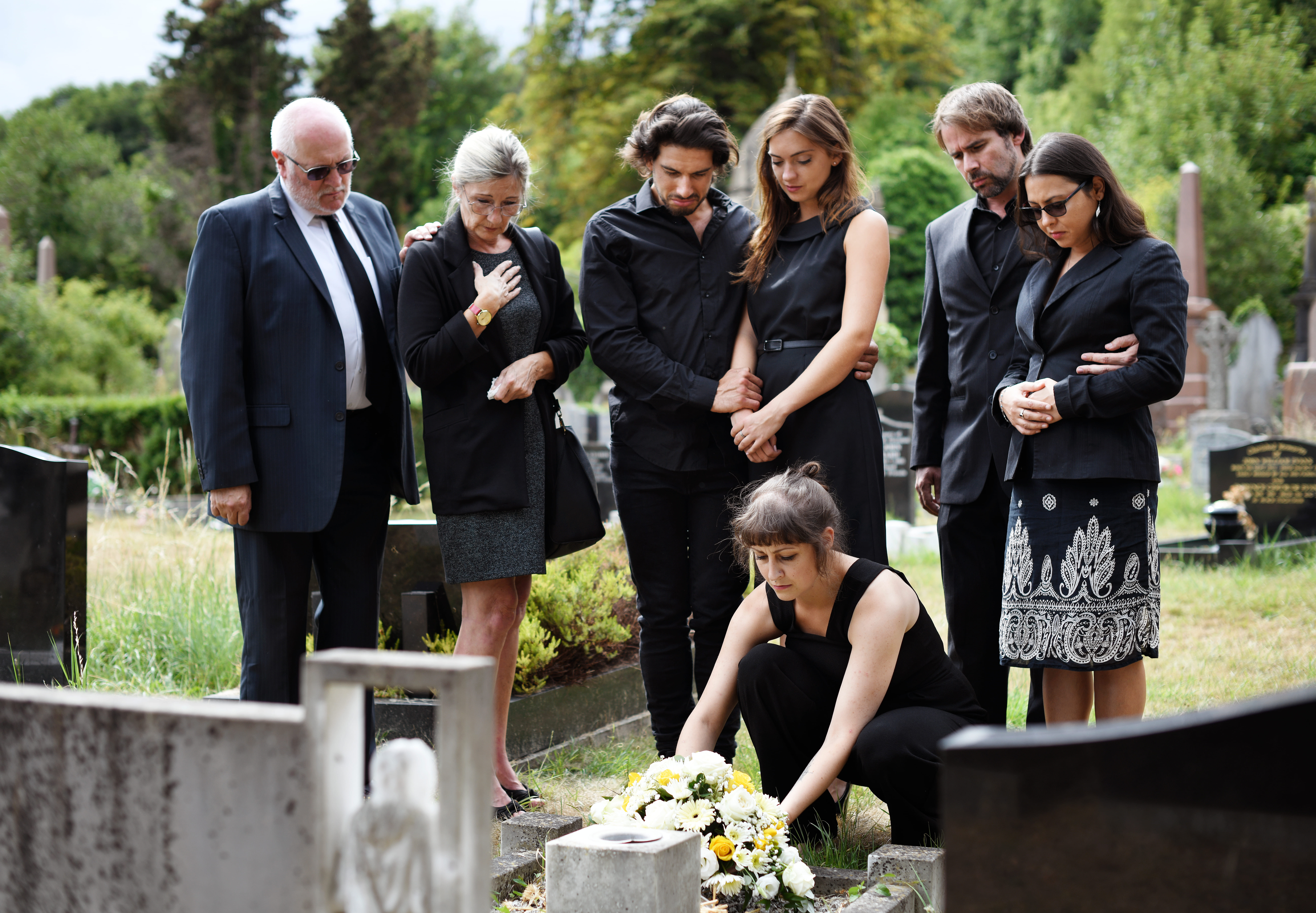 Famille déposant des fleurs sur la tombe dans un cimetière | Source : Shutterstock