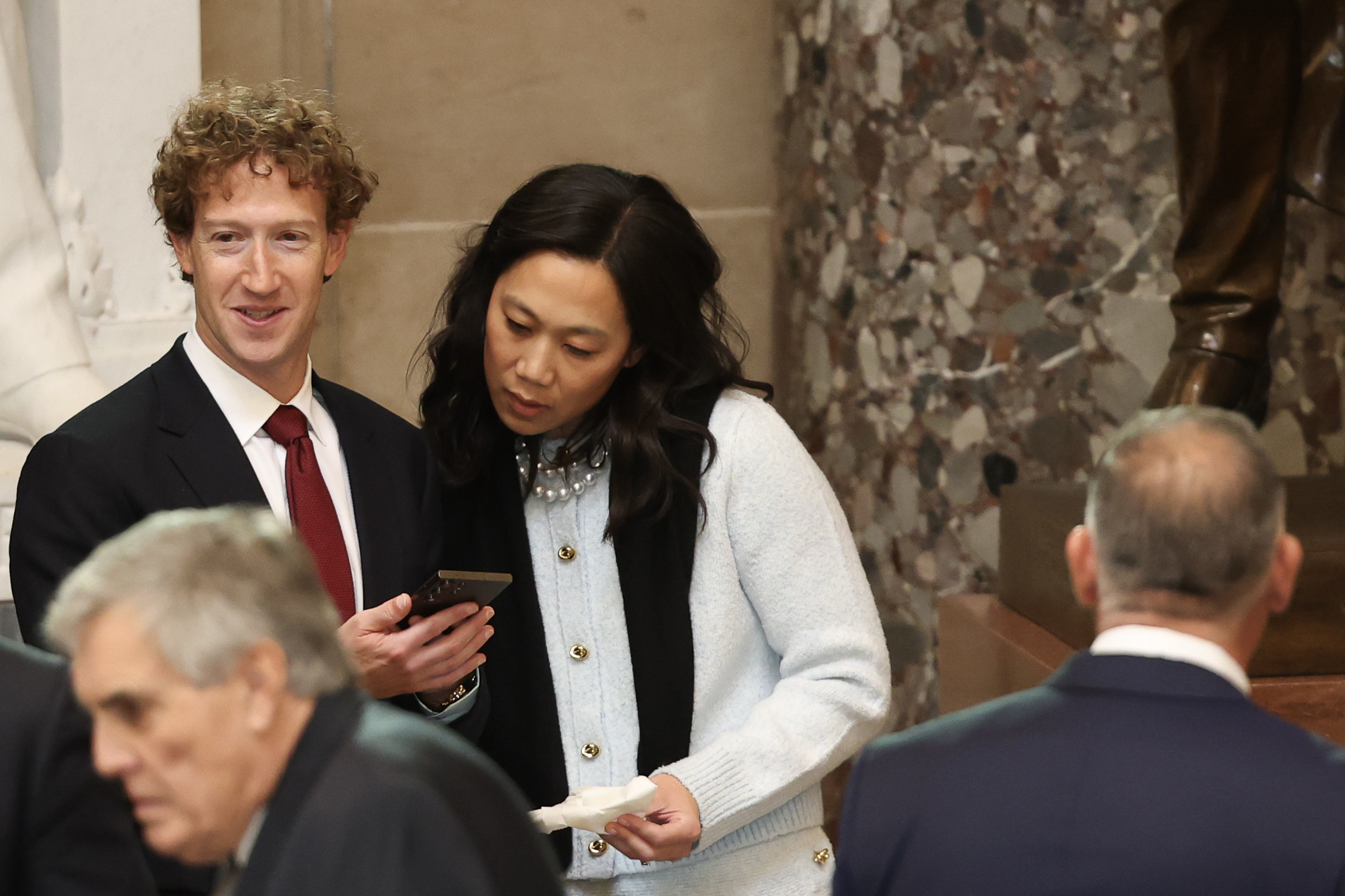 Priscilla Chan regardant le téléphone de Mark Zuckerberg alors qu'ils se tiennent l'un à côté de l'autre pendant l'investiture de Donald Trump. | Source : Getty Images