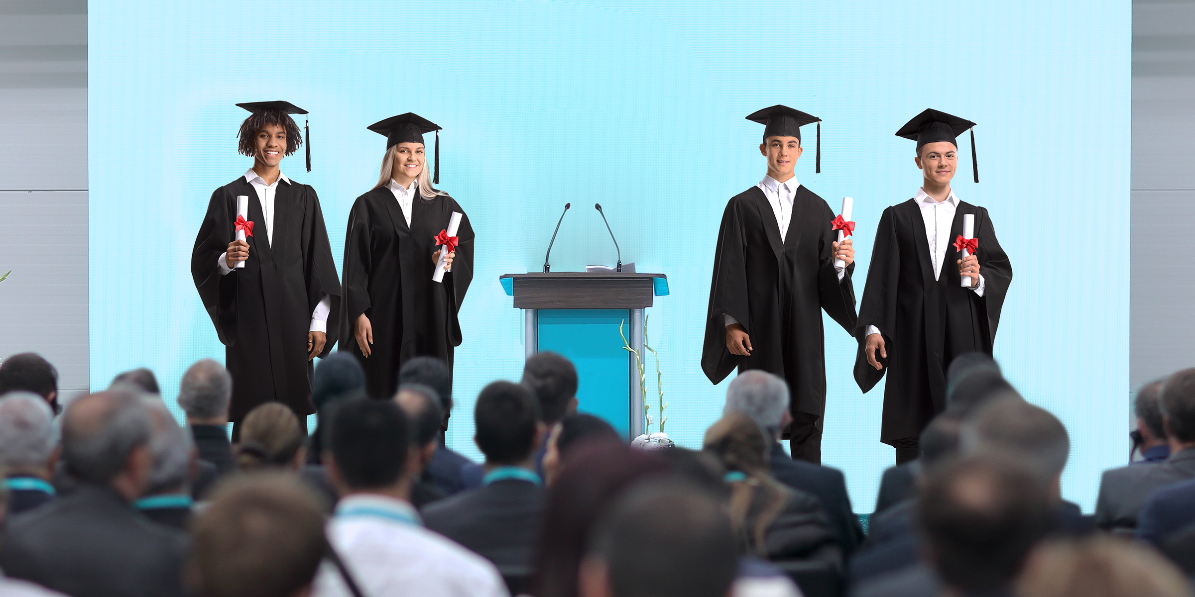 Des diplômés en casquette et robe tiennent fièrement leurs diplômes sur scène sous le regard du public | Source : Shutterstock