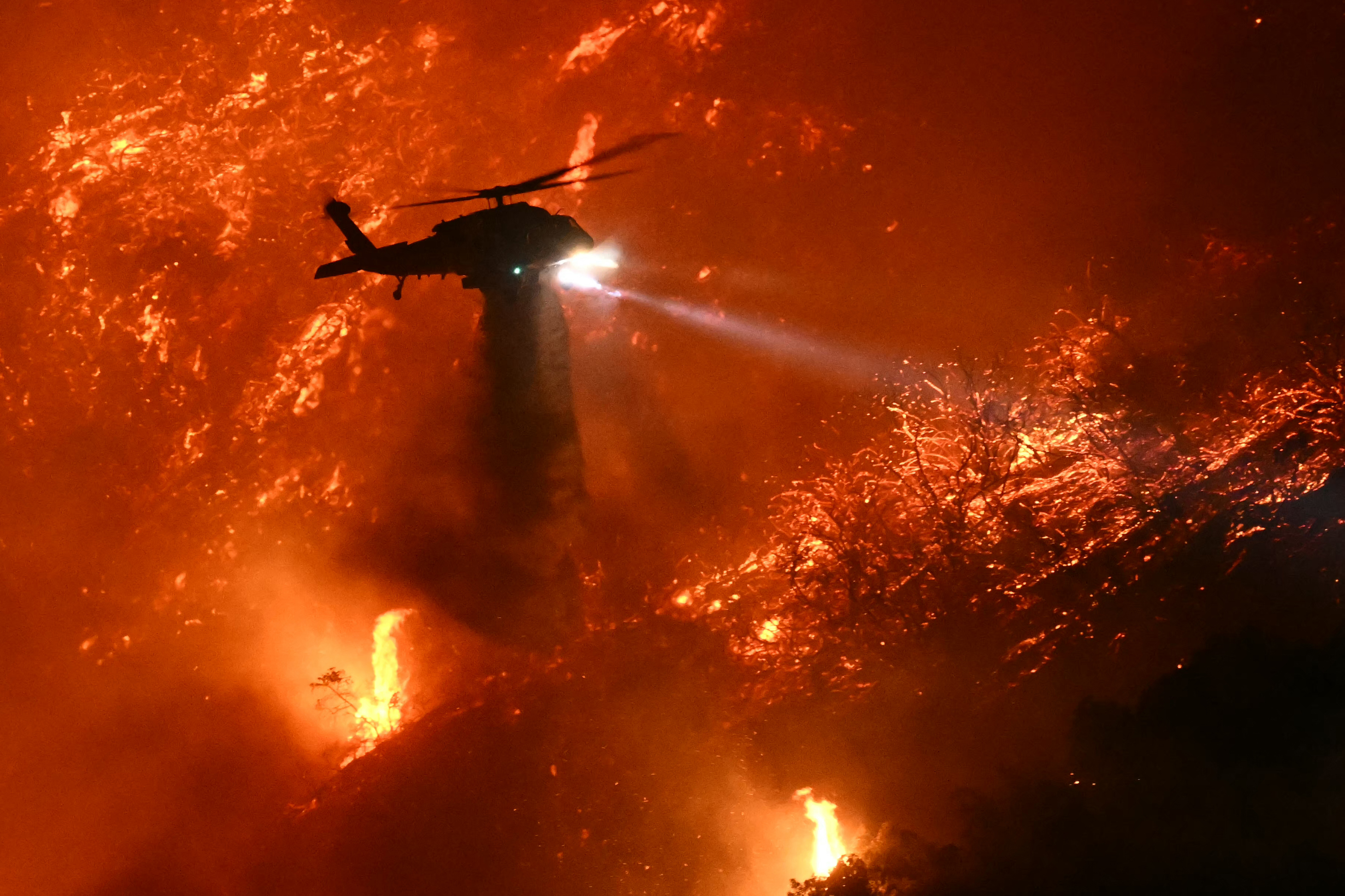 Un hélicoptère de lutte contre les incendies largue de l'eau alors que l'incendie de Palisades prend de l'ampleur près du quartier de Mandeville Canyon et d'Encino, en Californie, le 11 janvier 2025 | Source : Getty Images