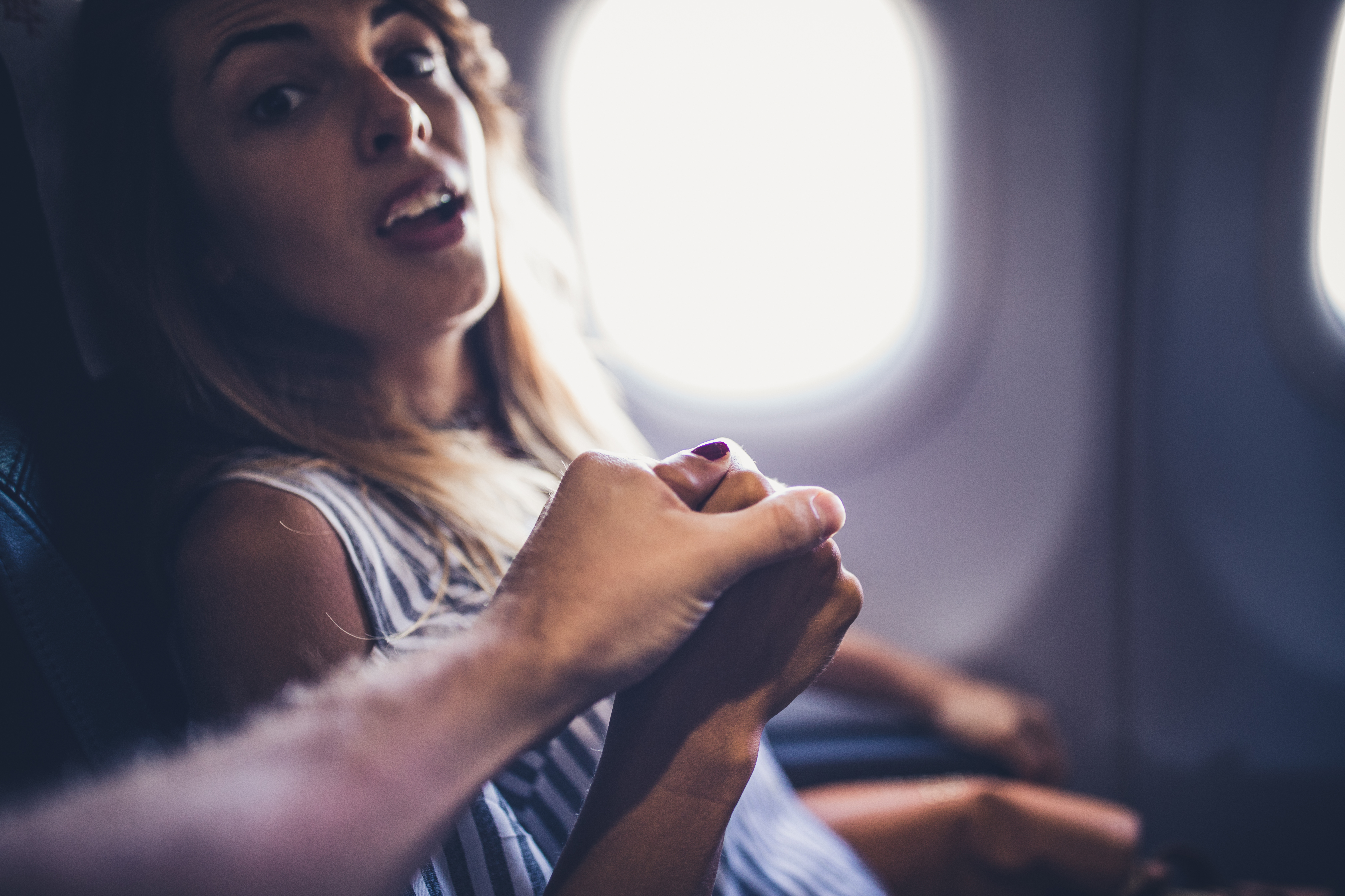 Un mari tient la main de sa femme effrayée dans un avion | Source : Getty Images