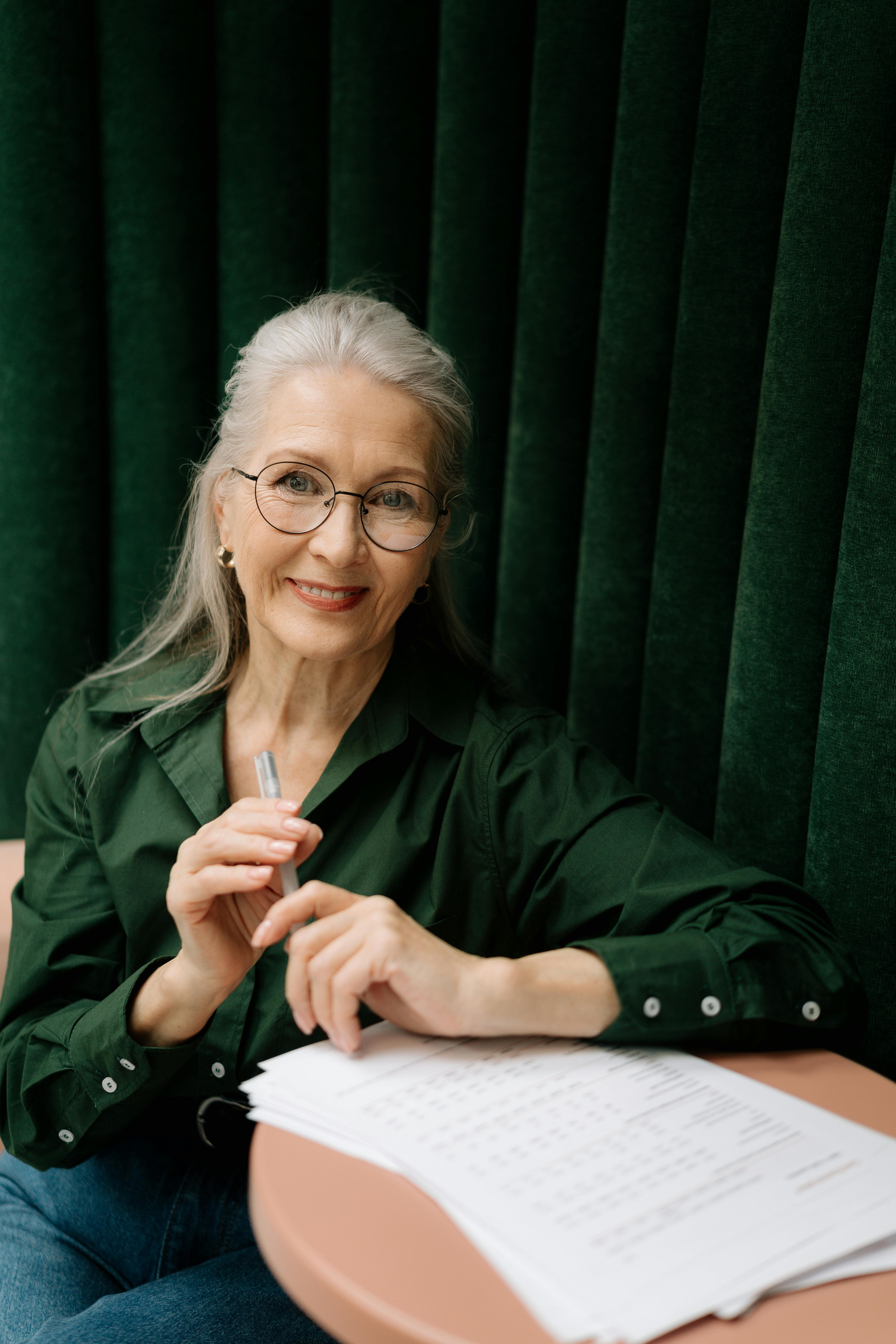 Une femme âgée souriante assise à une table | Source : Pexels