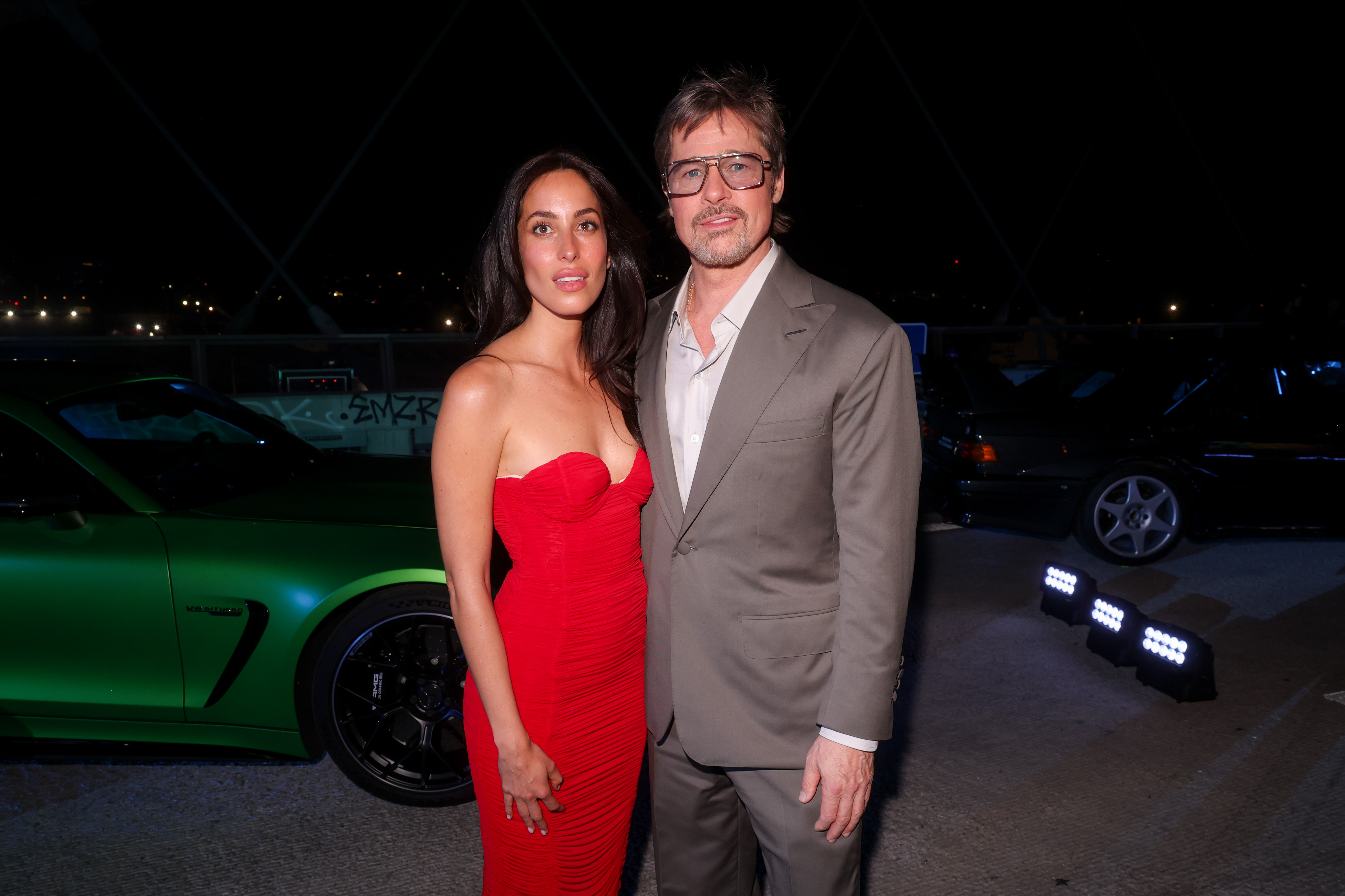 Ines de Ramon pose aux côtés de Brad Pitt devant une Mercedes-AMG verte, renforçant ainsi l'ambiance de course automobile haut de gamme qui règne lors de cette avant-première glamour.