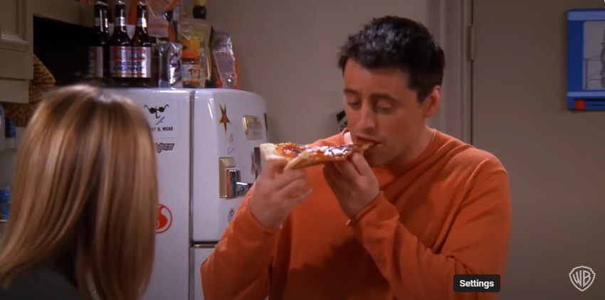 Matt LeBlanc dans le rôle de Joey sur le plateau de "Friends" mangeant une pizza | Source : YouTube/@warnerbrostv