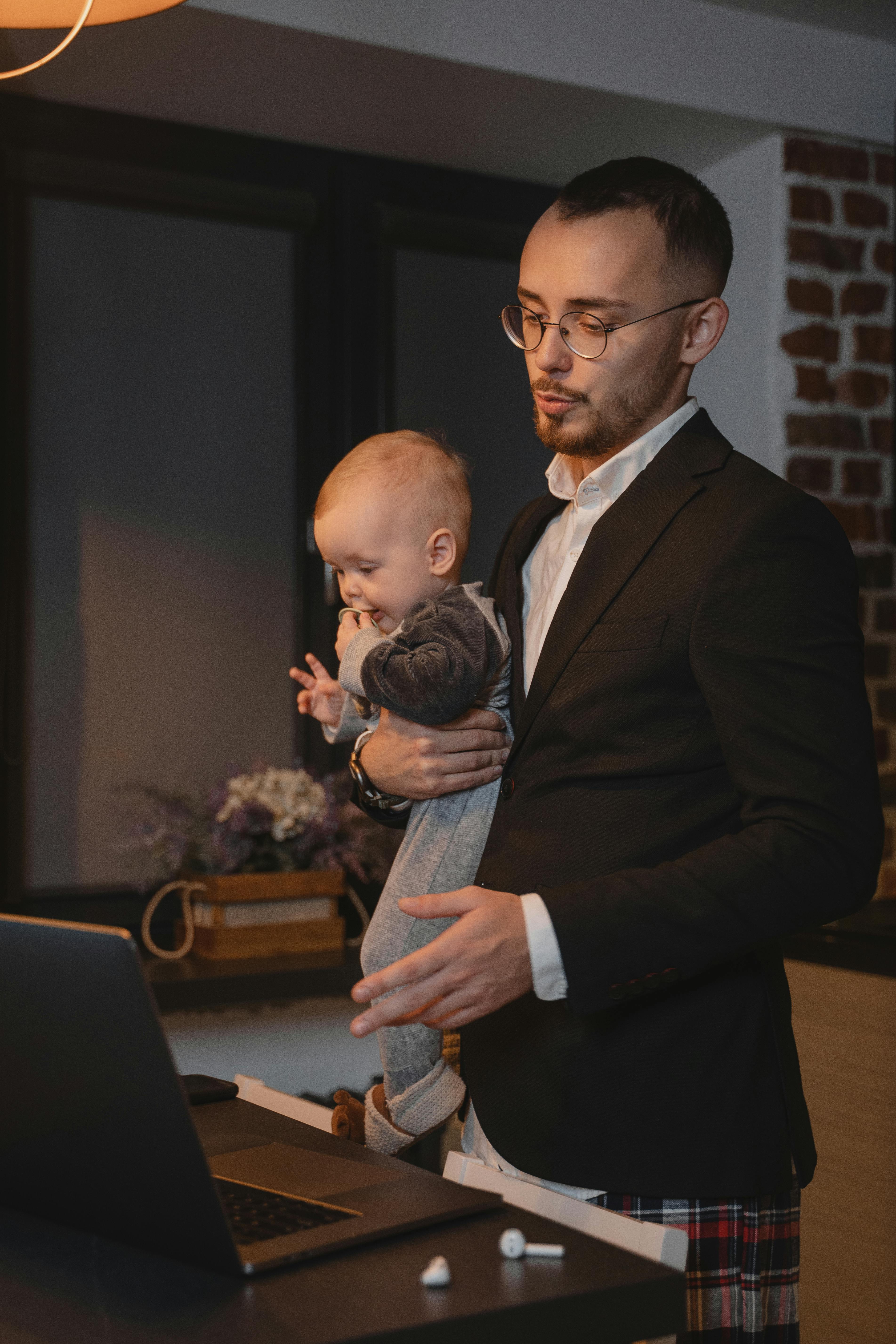Un père portant un bébé tout en étant sur son ordinateur portable | Source : Pexels