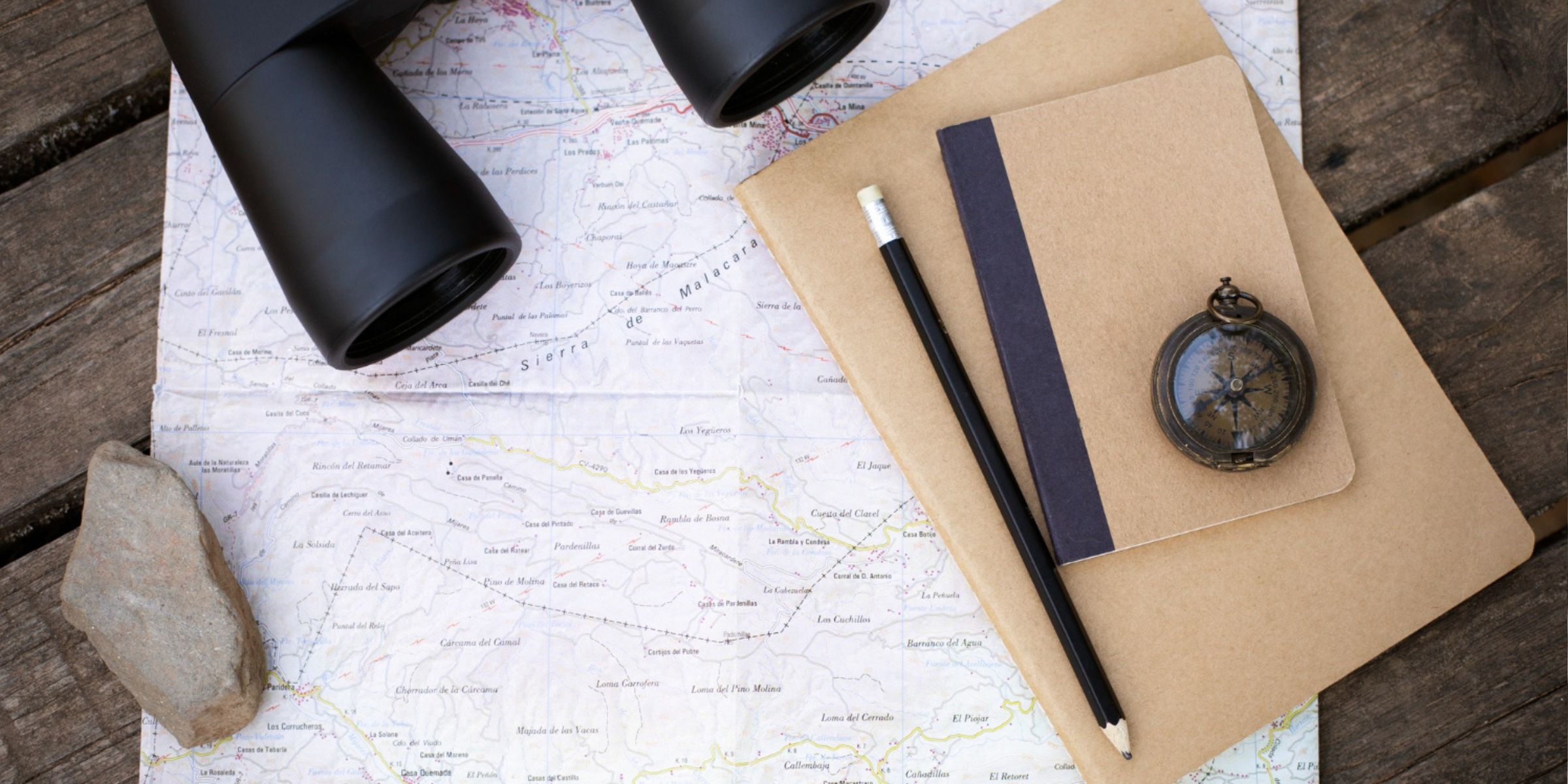 Une carte, un carnet et une boussole posés à côté de jumelles | Source : Magnific