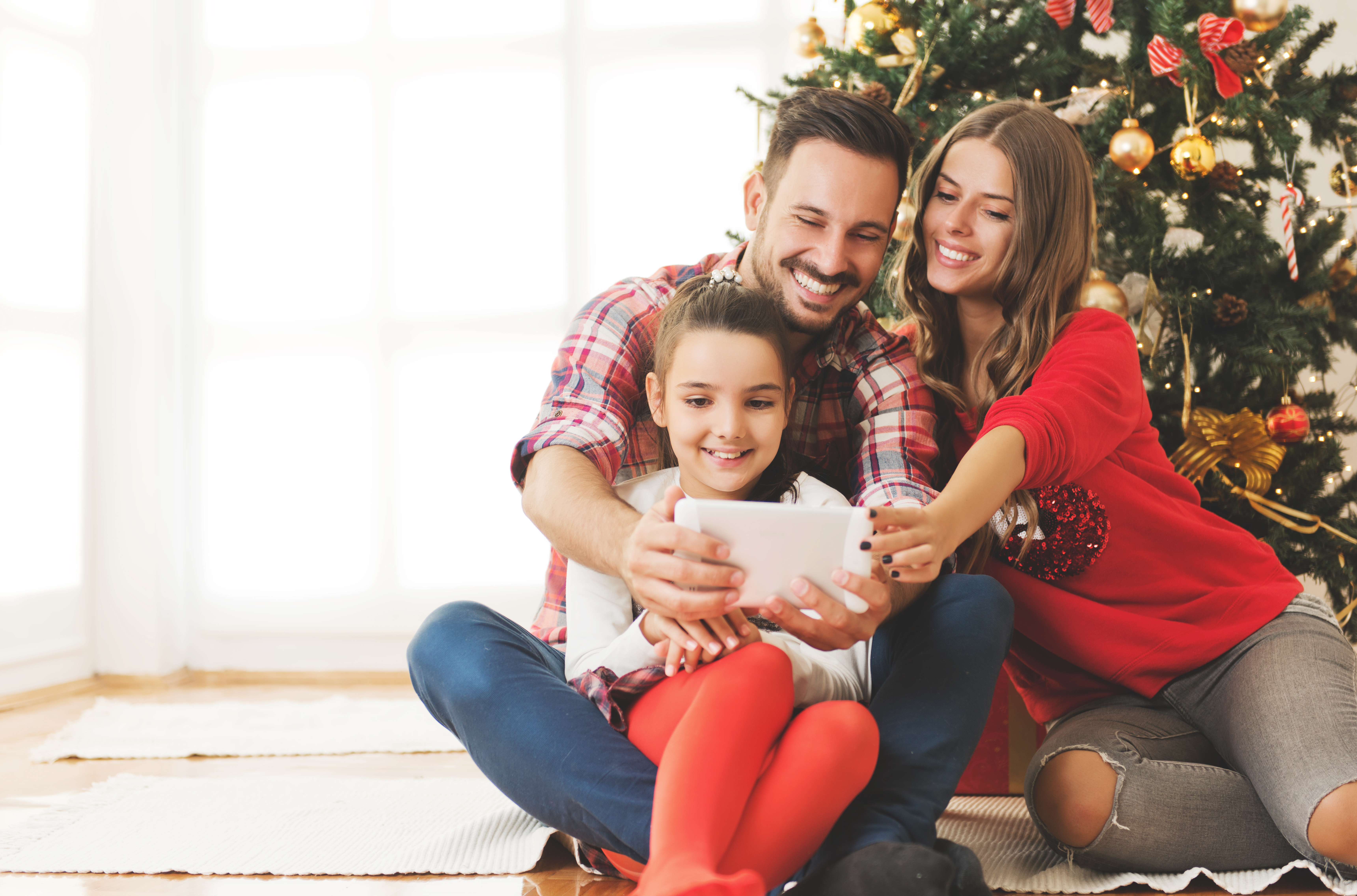Une petite fille jouant avec un iPad en compagnie de son père et de sa mère avec un sapin de Noël en arrière-plan | Source : Shutterstock